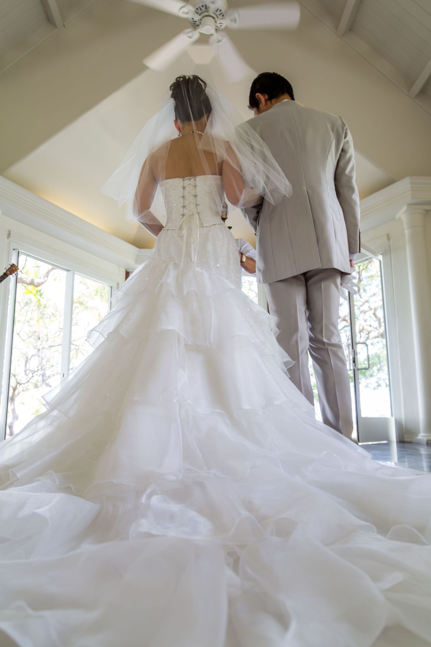 A dramatic back view of a bride and groom standing under a white ceiling with a flowing wedding dress train.