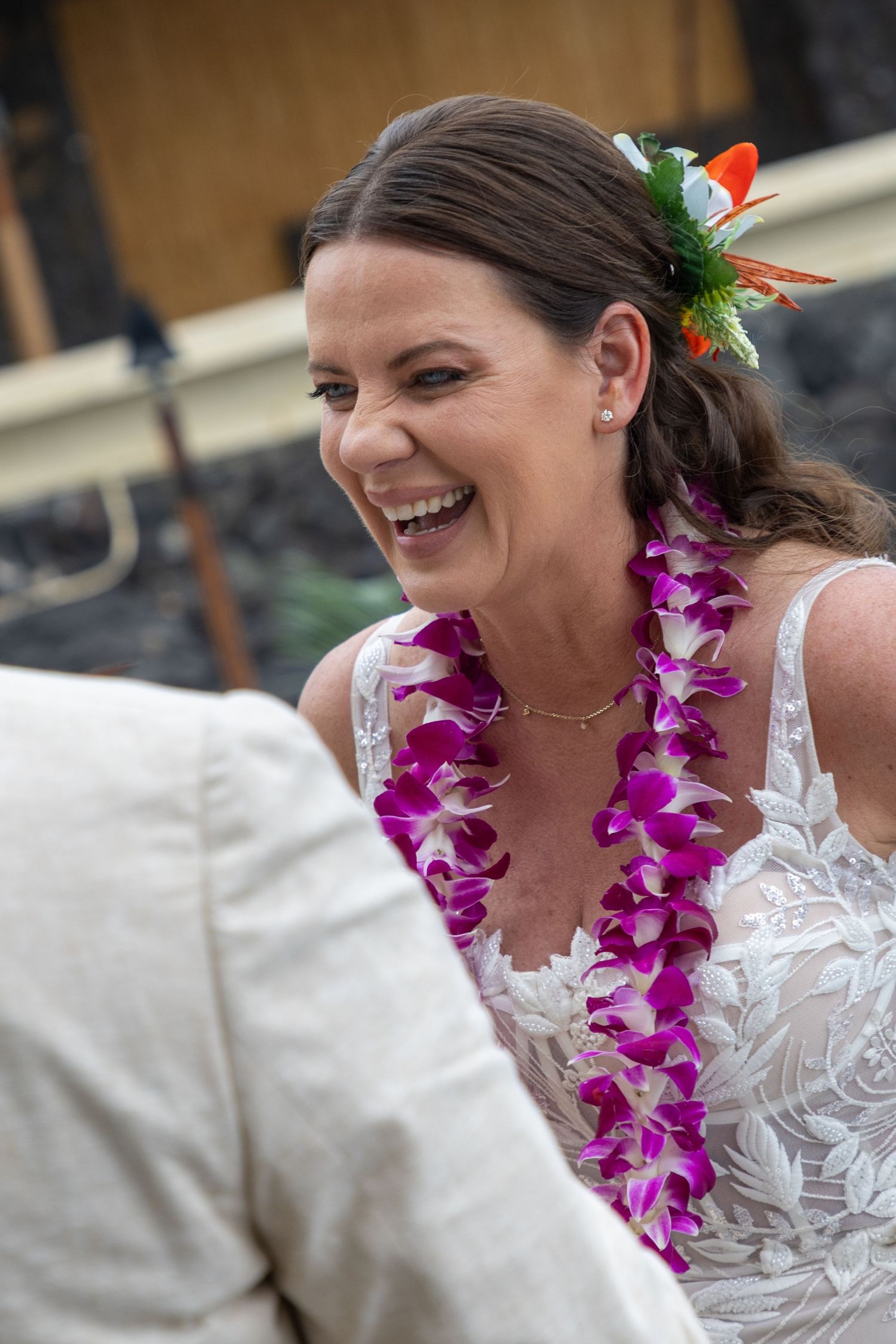 Bride laughing joyfully wearing a purple orchid lei and floral hair accessory at a Hawaiian wedding ceremony.