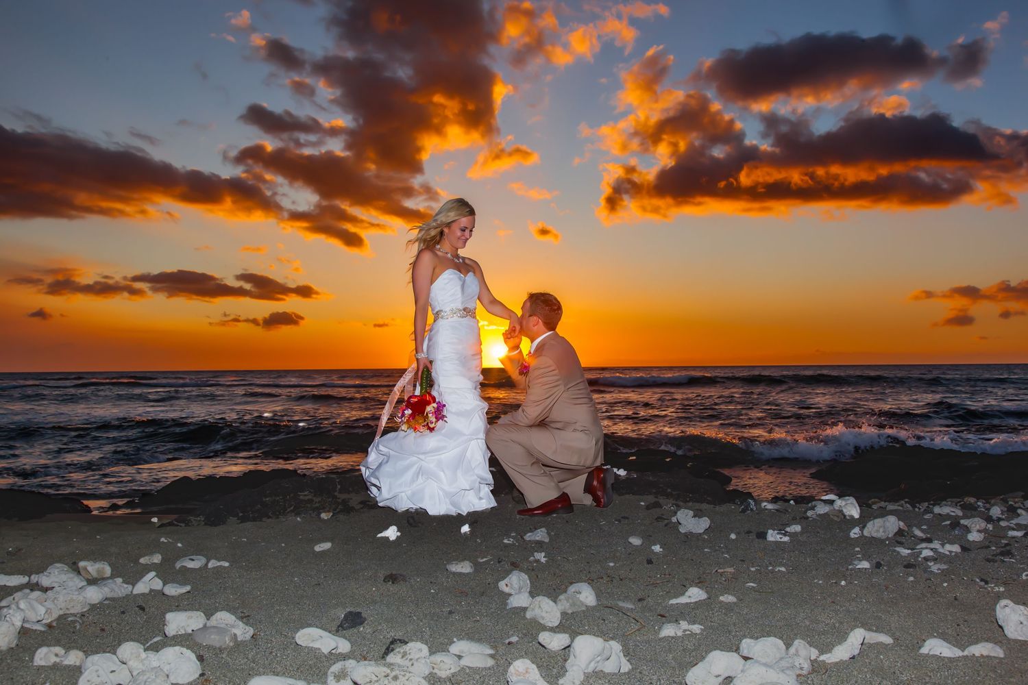 A Romantic portrait of a wedding couple against a vibrant orange sunset over the ocean at the Mauna Lani beach near Kailua Kona, Hawaii.