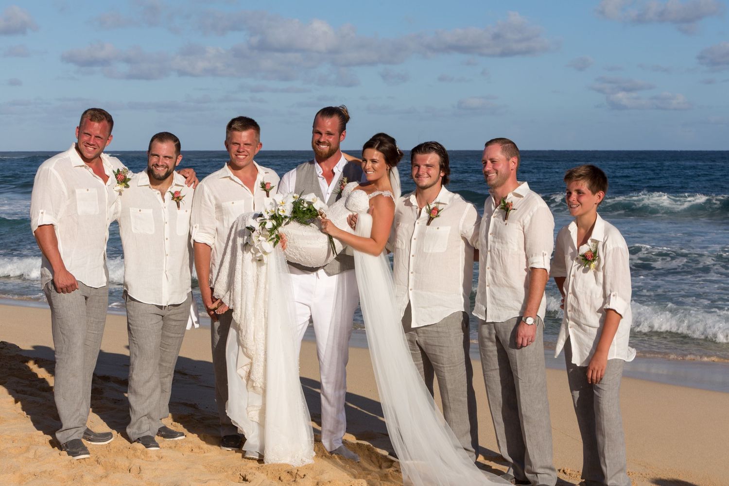 Beach wedding party photo with bride in white and groomsmen in casual white shirts in Kauai.