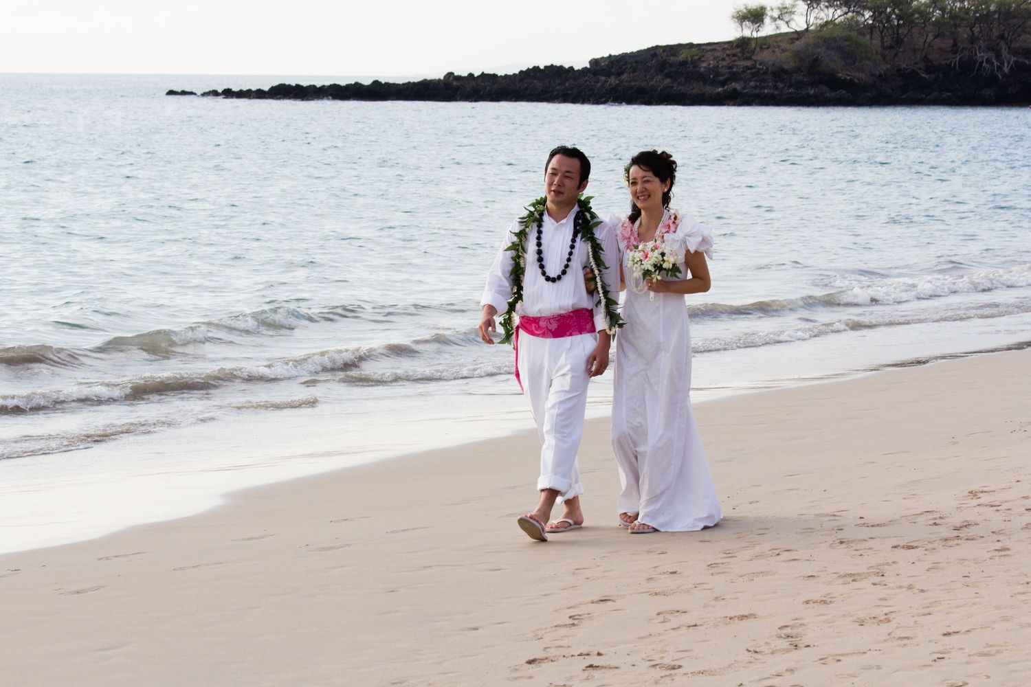 A couple walking on a Kailua Kona beach, a popular spot for professional portrait photography with scenic lava rocks