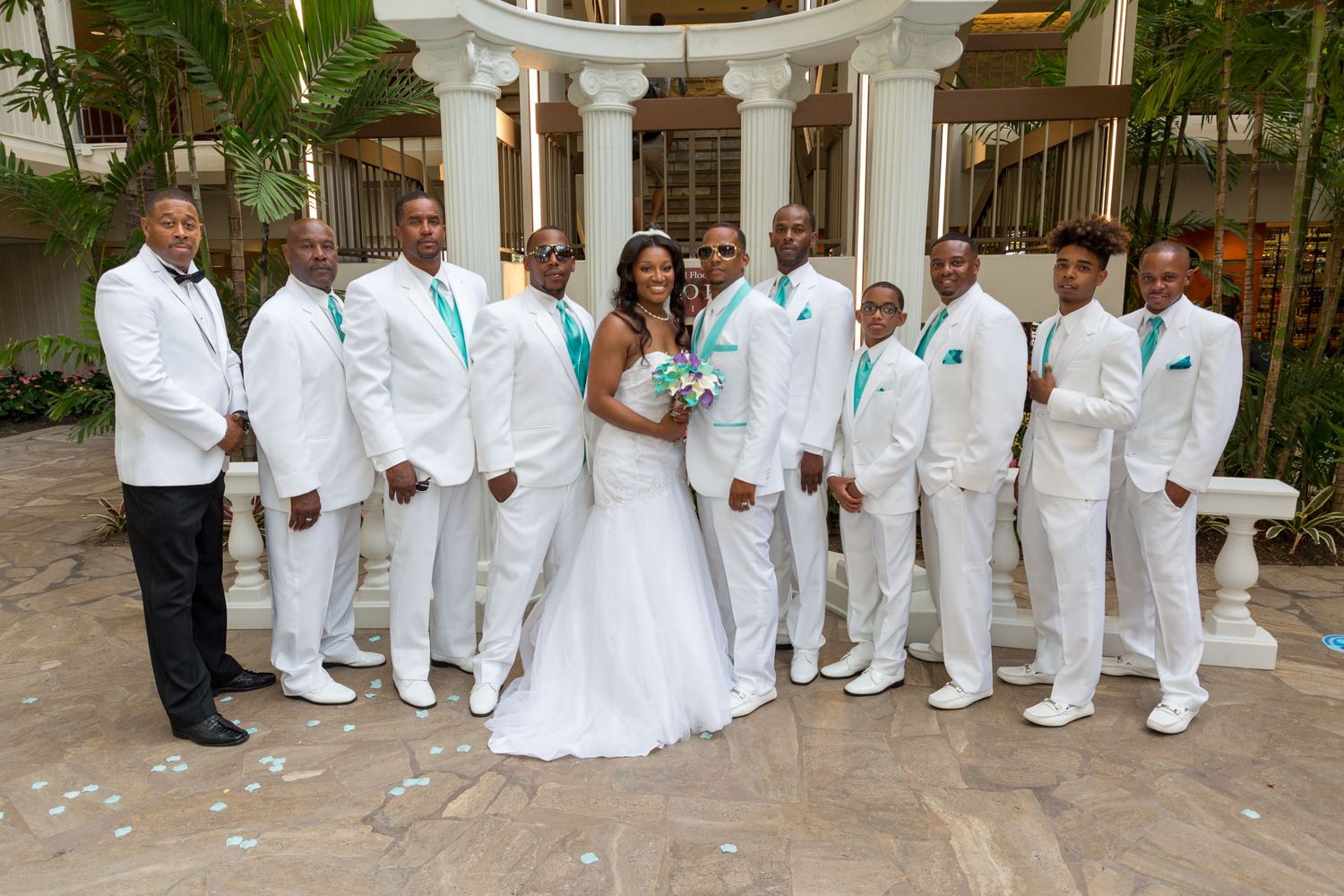 Wedding party in crisp white attire poses under elegant columned gazebo.