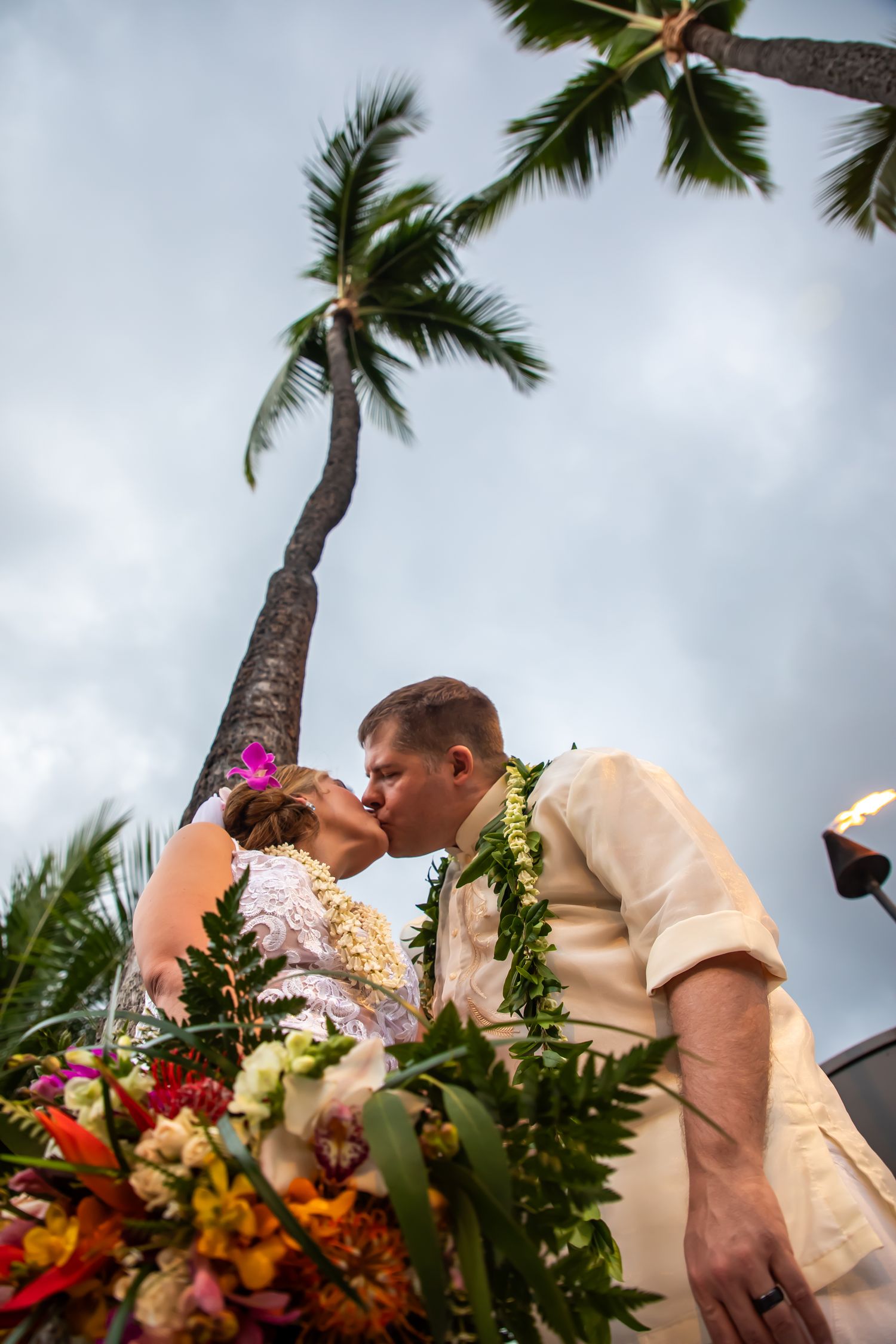 A romantic tropical wedding moment captured under swaying palm trees with vibrant floral arrangements and Hawaiian leis.