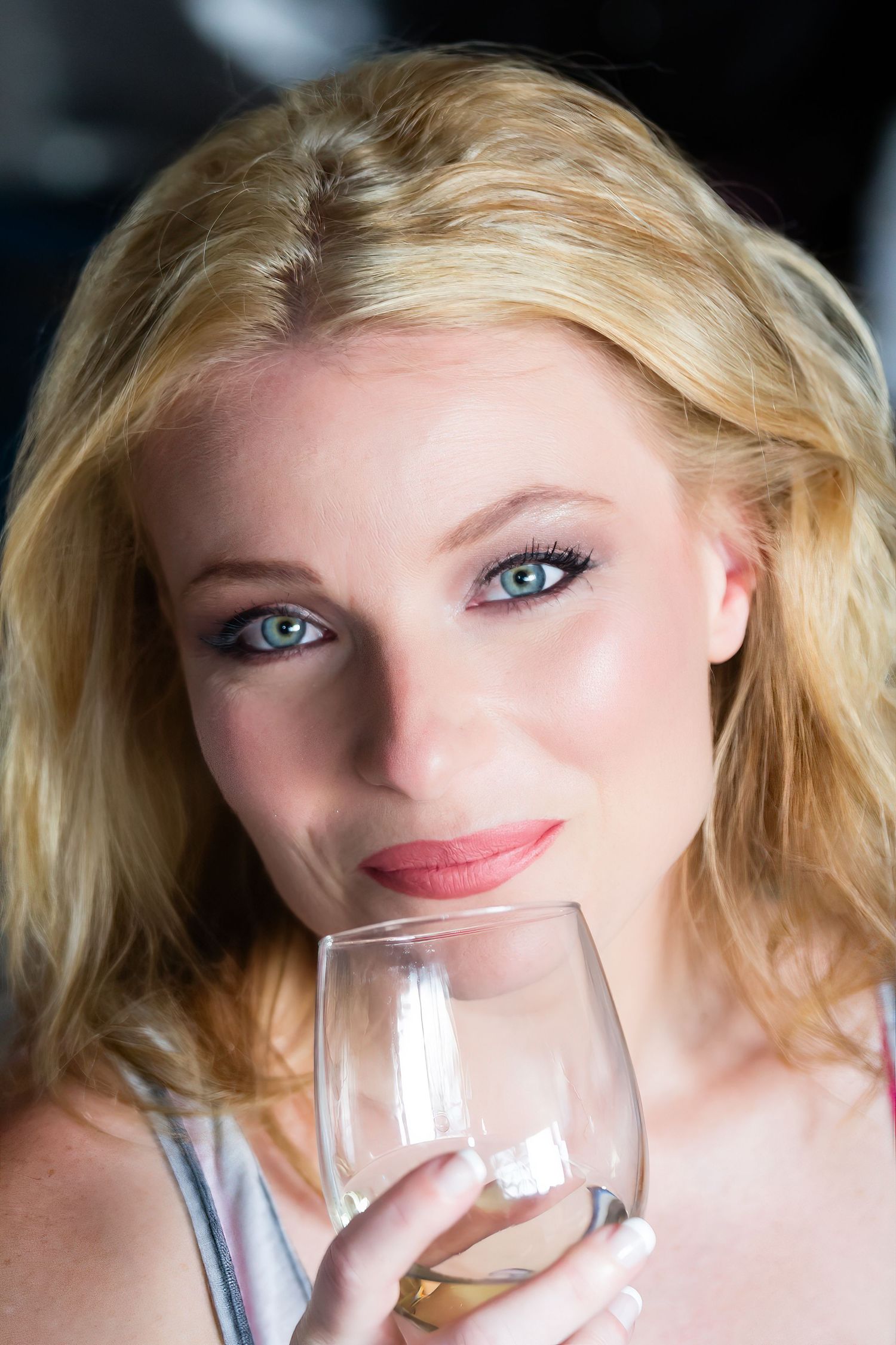 Person with blonde hair and blue eyes takes several sips from a clear drinking glass in sequence.