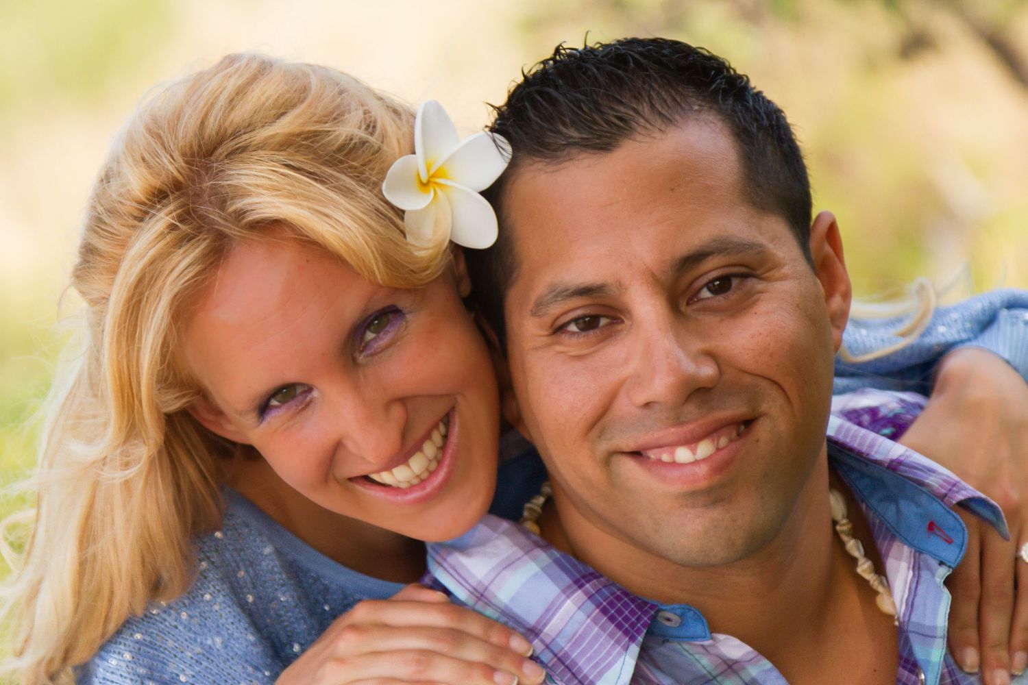 Happy couple smiling together outdoors with warm sunlight and white flower in hair.