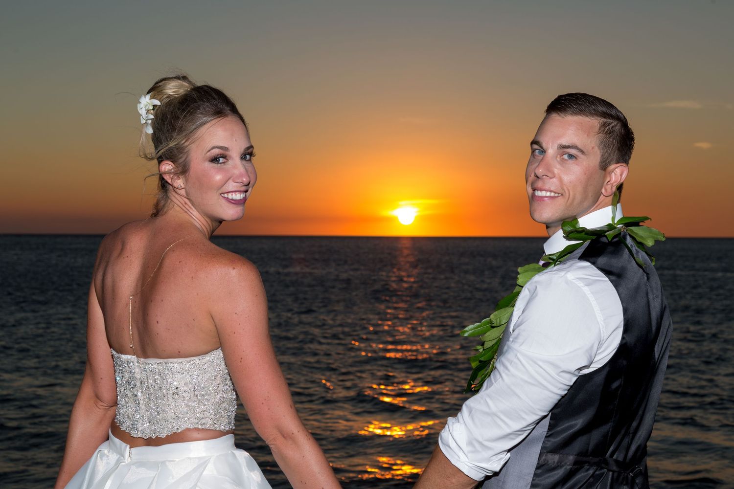 Bride and groom posing together at a stunning ocean sunset during their Hawaiian beach wedding ceremony.