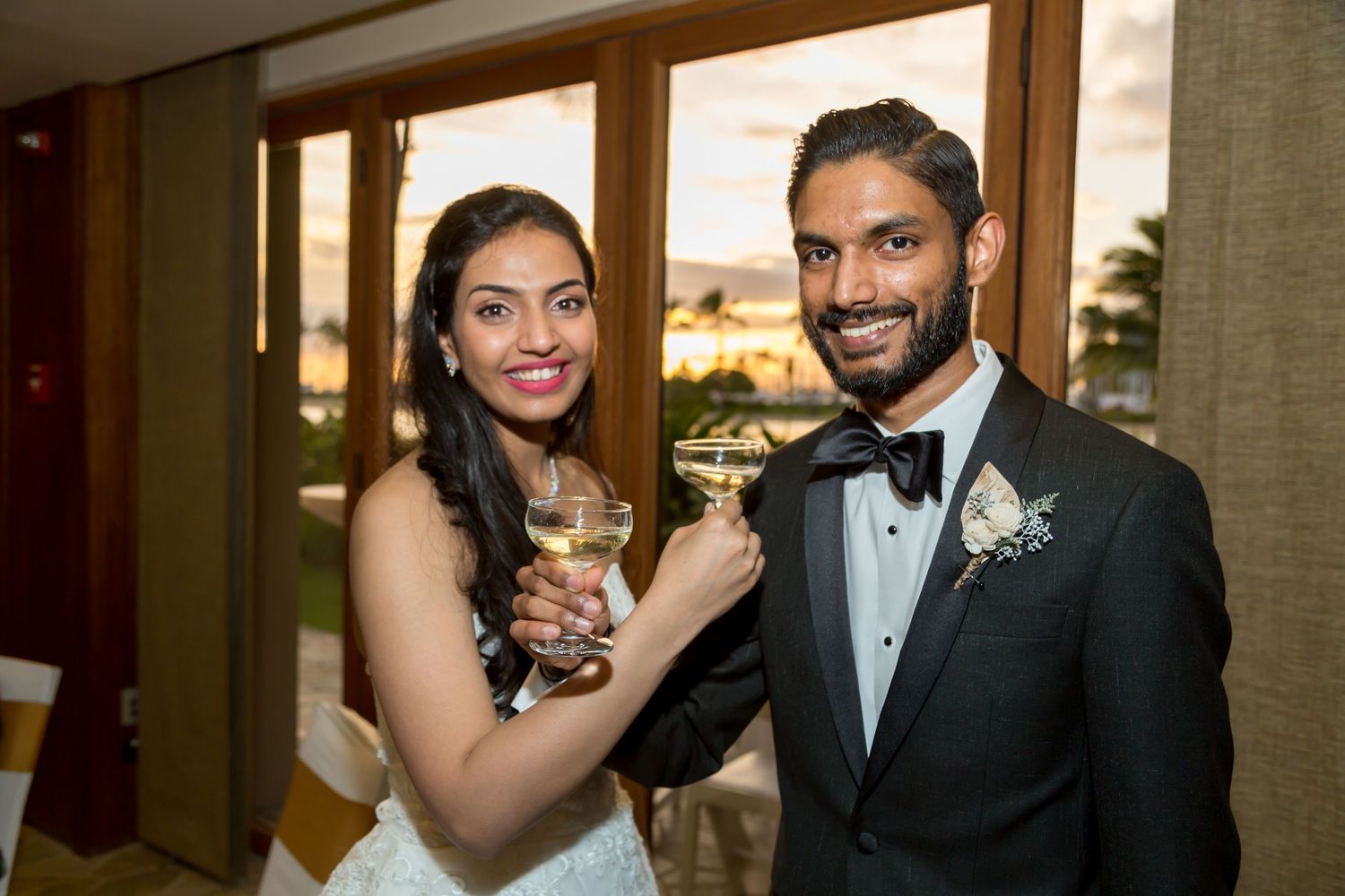 Bride and groom in wedding attire toasting with champagne glasses at their elegant indoor wedding reception.