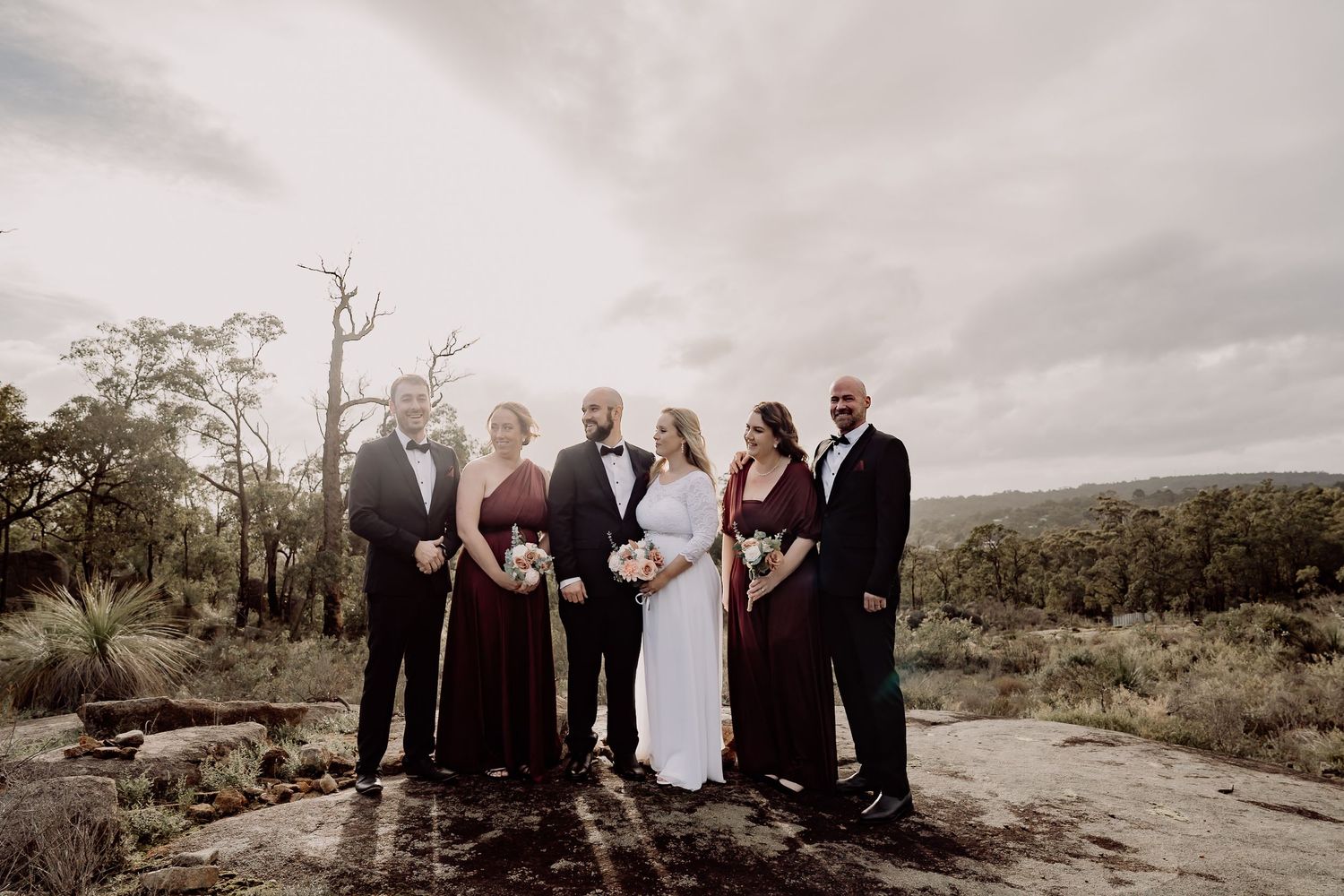 A wedding party poses together in a scenic desert landscape with mountains and cloudy skies in the background.