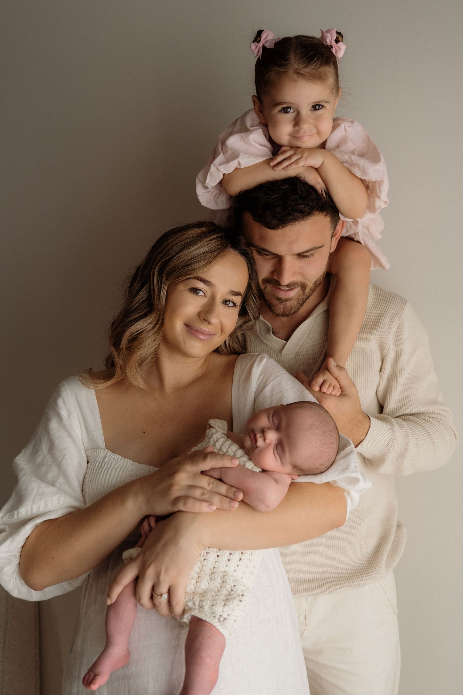 A couple in white clothing poses together in an intimate indoor studio photo session with soft lighting and neutral backdrop.
