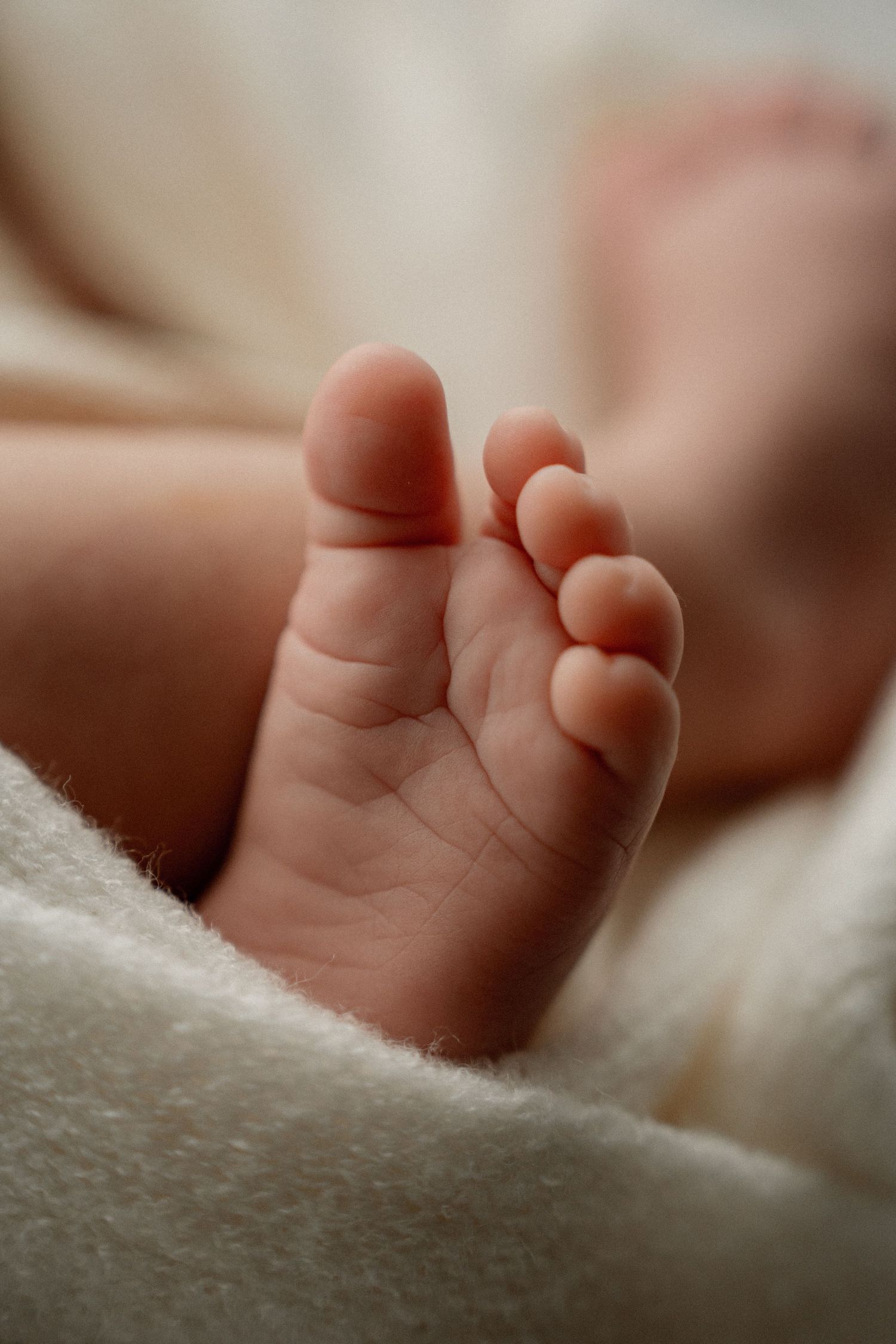 Close up macro shot of tiny newborn baby foot resting on soft white blanket in natural lighting.