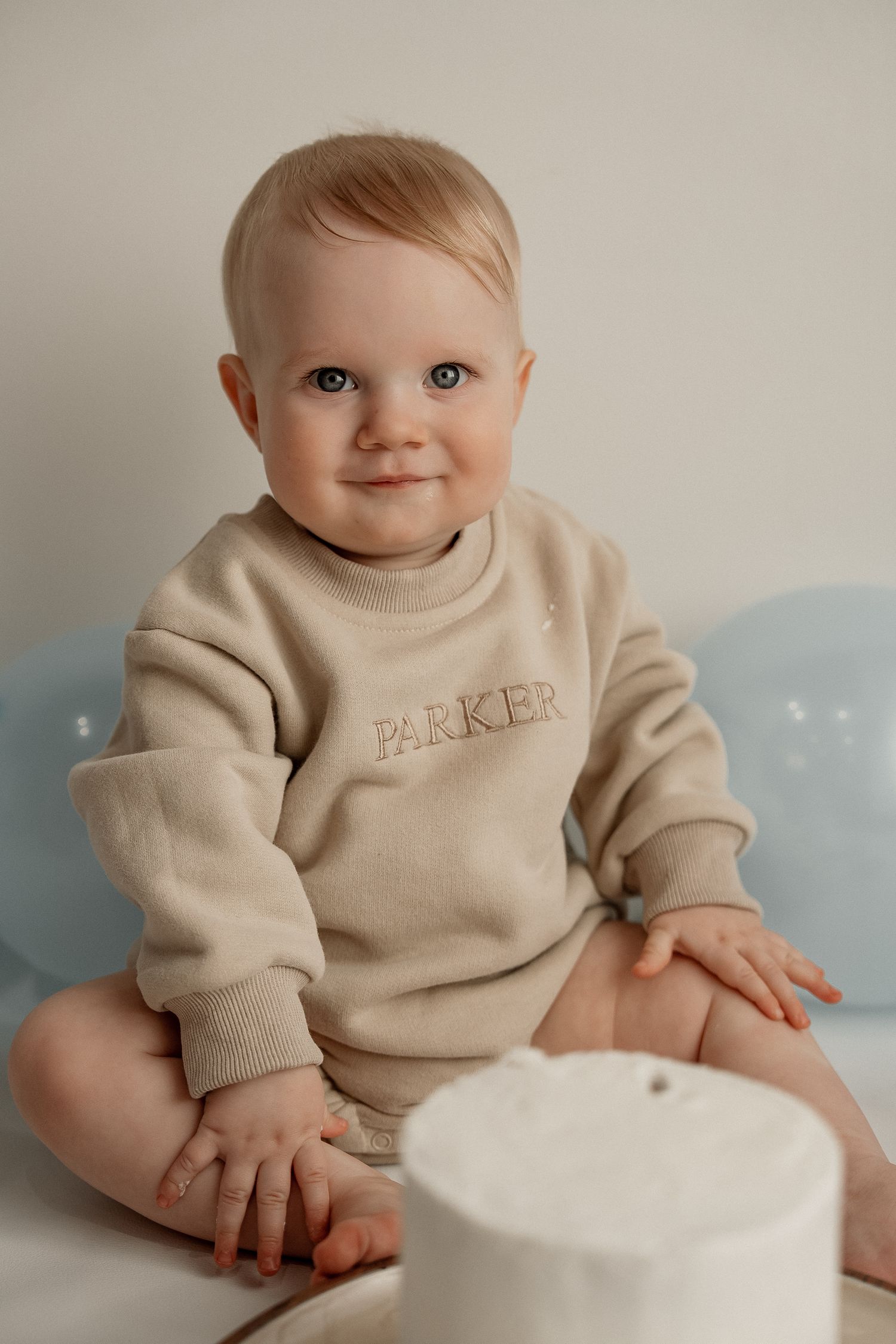 Baby in beige sweater sits on white surface with gentle smile in series of connected photos.