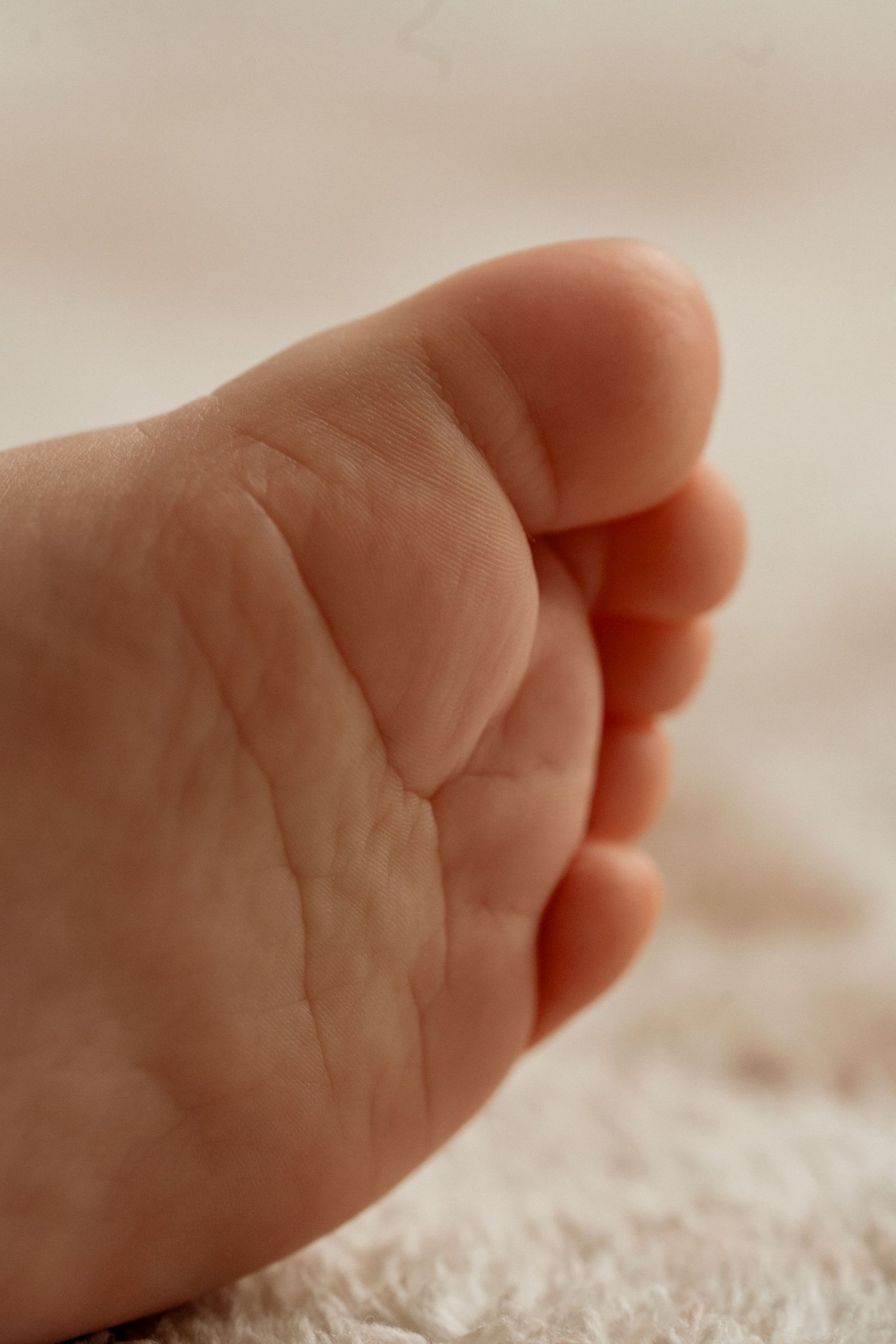 Close-up view of a tiny baby's hand resting on soft white fabric showing delicate skin details and wrinkles.