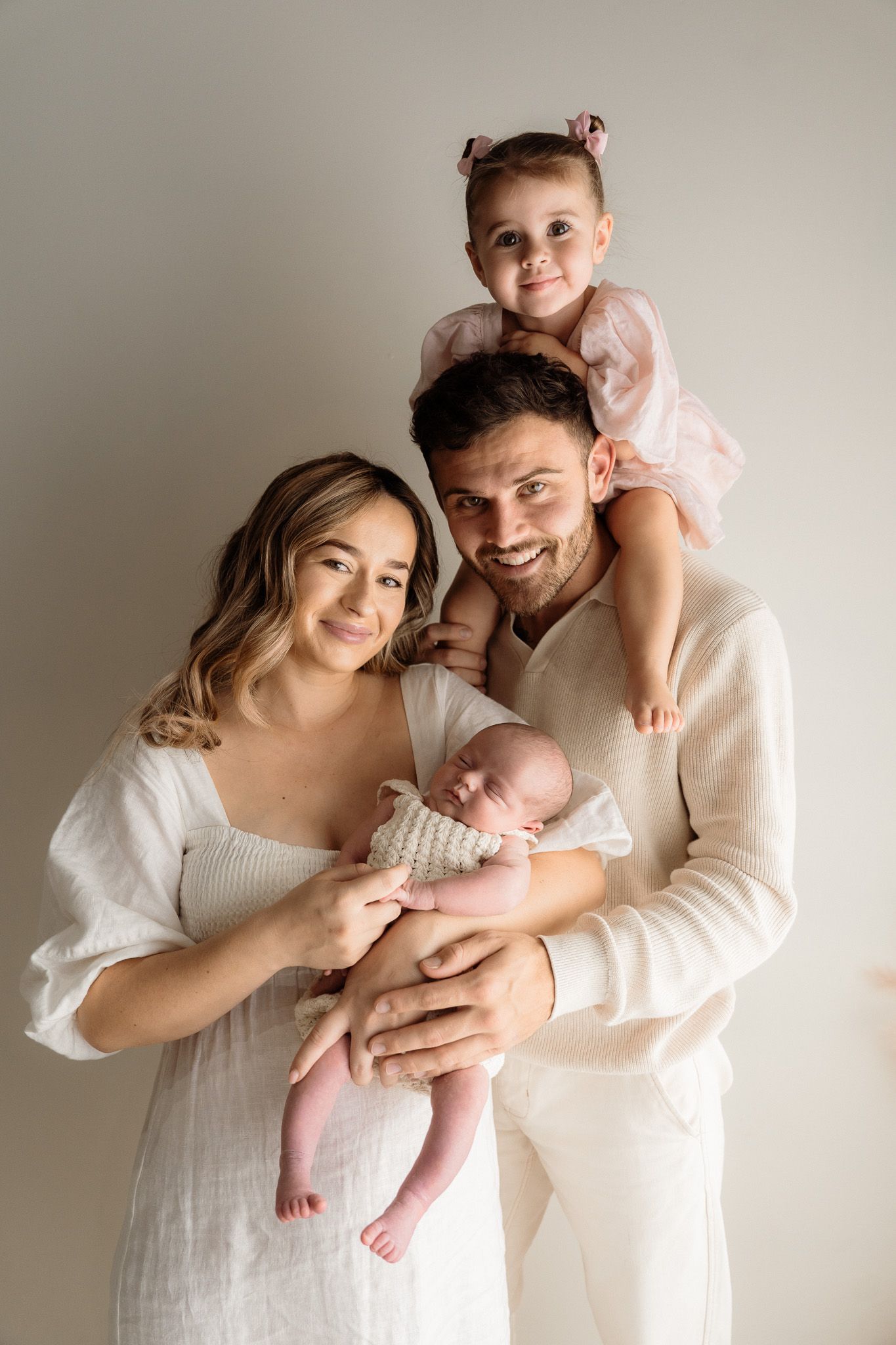 Family wearing white clothing poses together against neutral background in intimate lifestyle portraits.