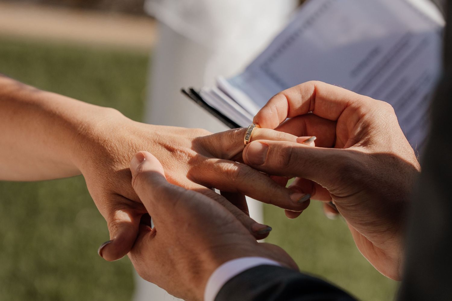 Close-up view of hands exchanging wedding rings during an outdoor ceremony.