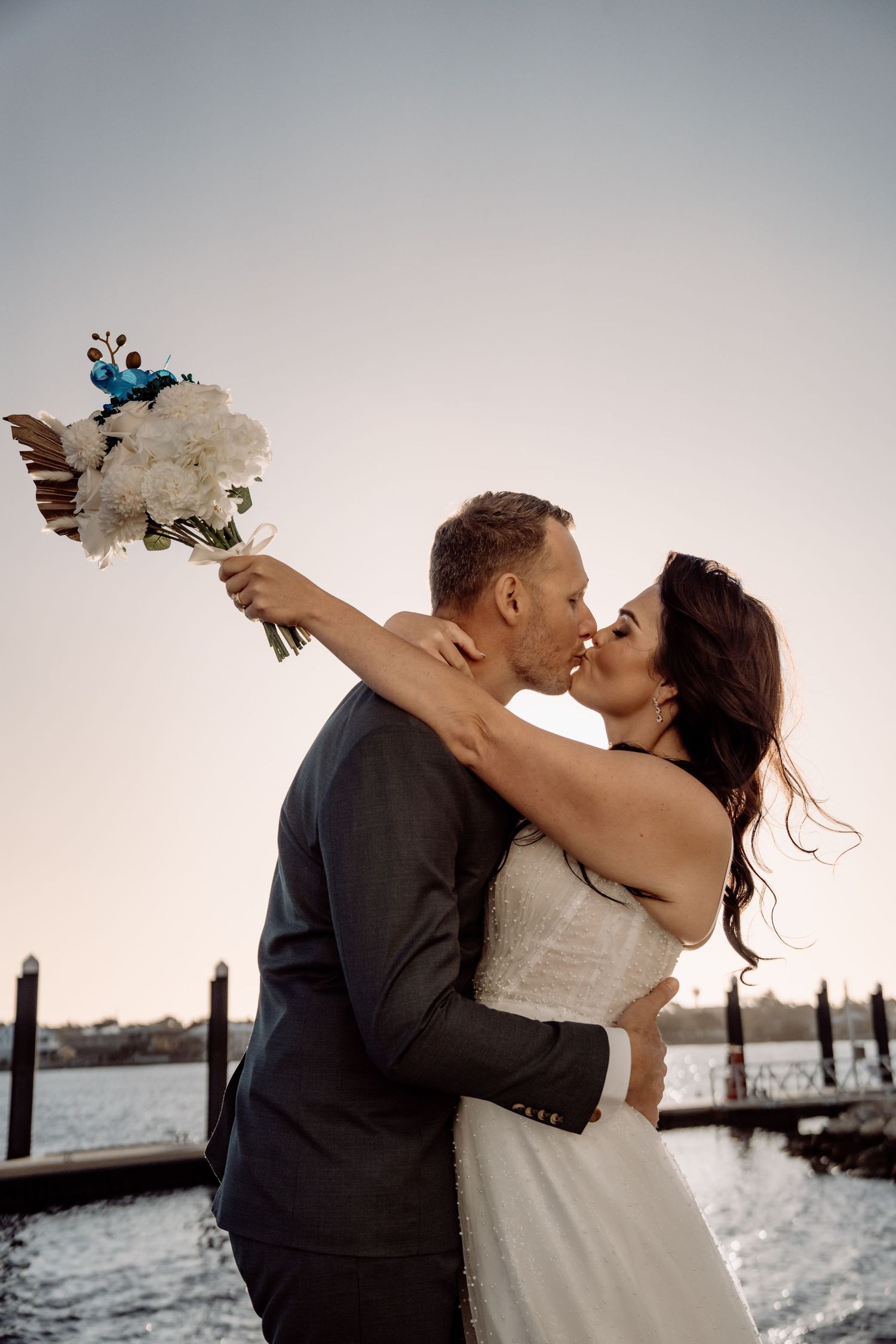 A couple shares romantic moments by the water in a series of black and white wedding photos at sunset.