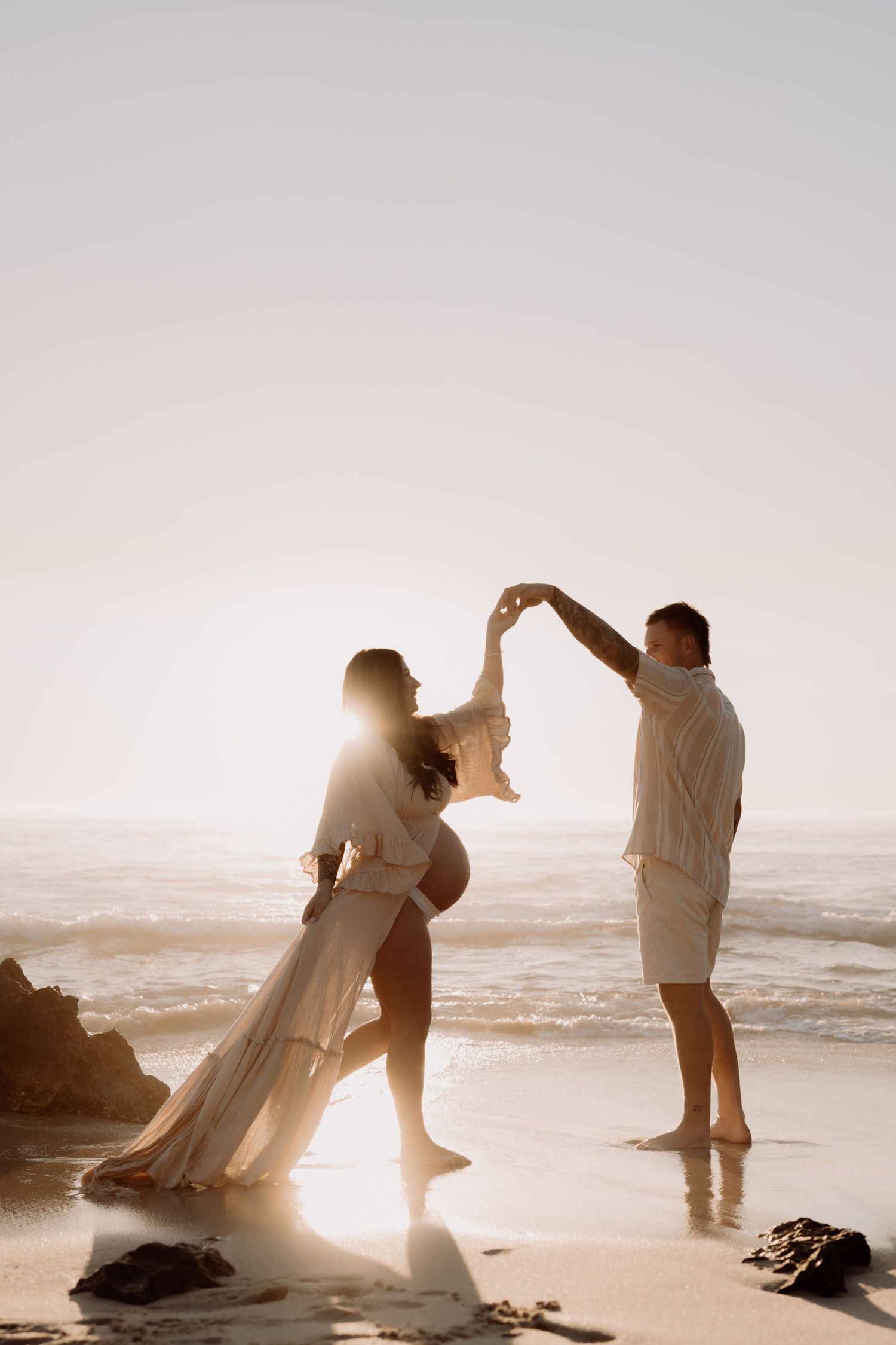 A romantic couple dances together on a sunlit beach at sunset creating silhouettes against the golden light.