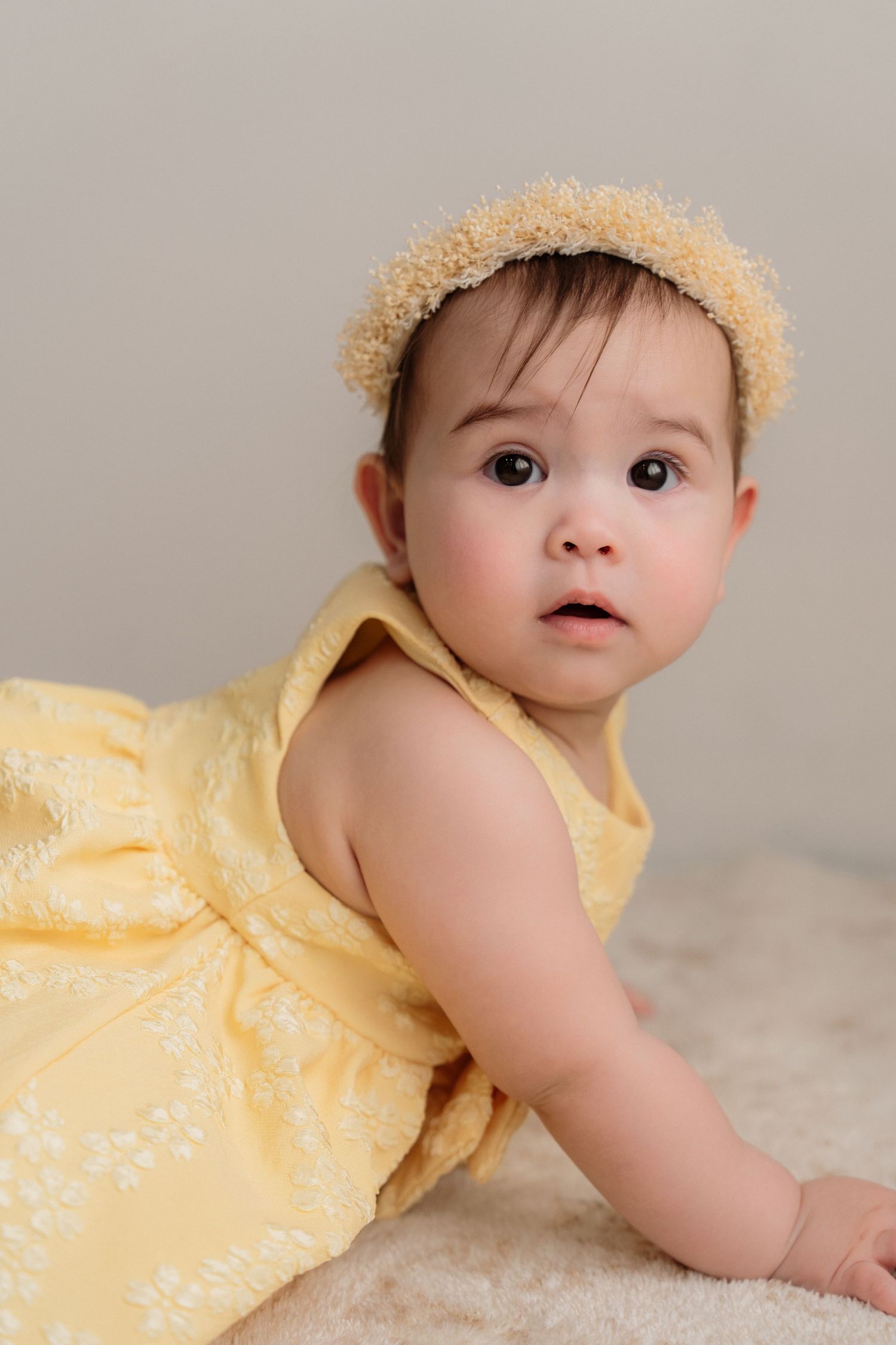 Baby in yellow dress and straw hat crawling on light colored floor in sequence of connected photos.