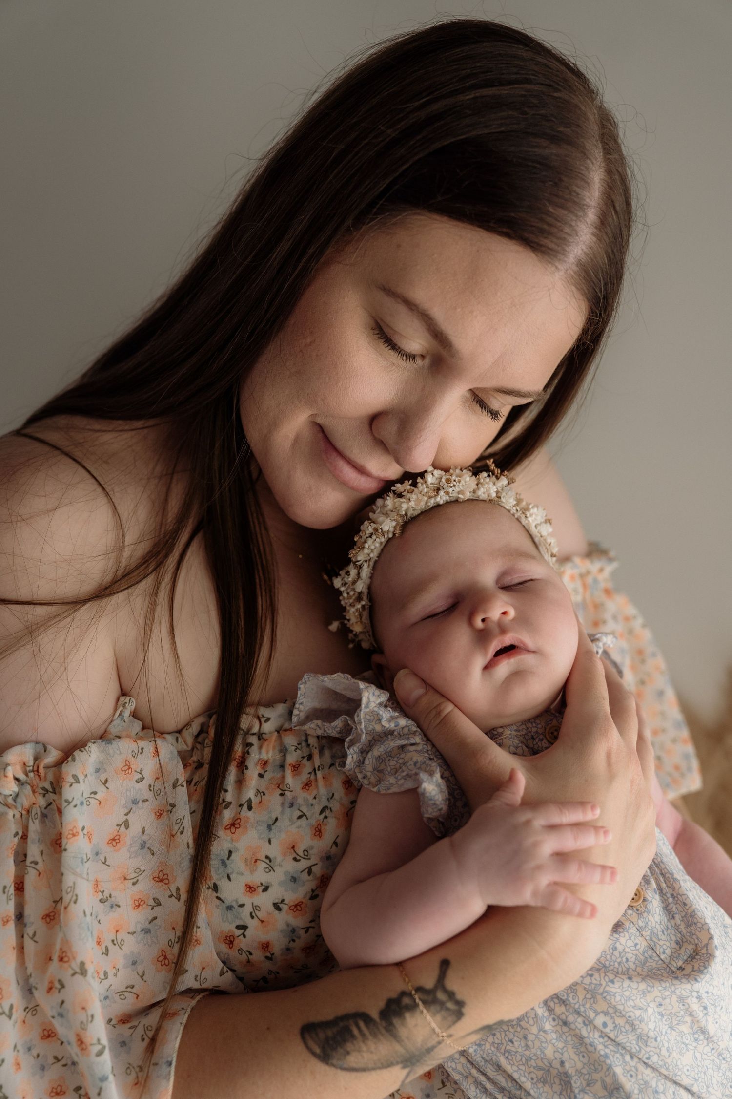 A tender portrait of a mother in a floral dress holding her sleeping newborn baby with a delicate lace headband.