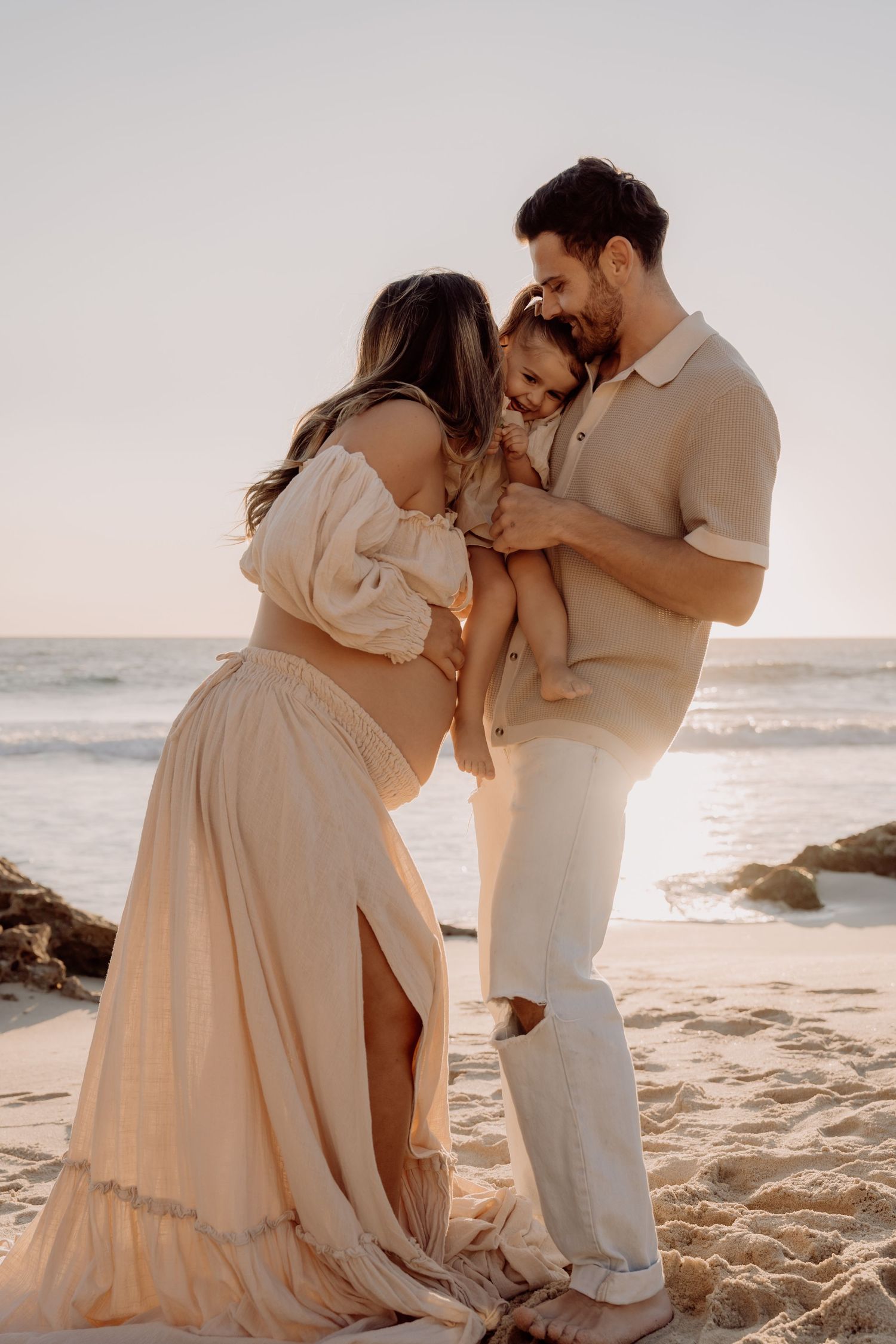 Intimate family moment captured on beach at sunset in neutral toned clothing.
