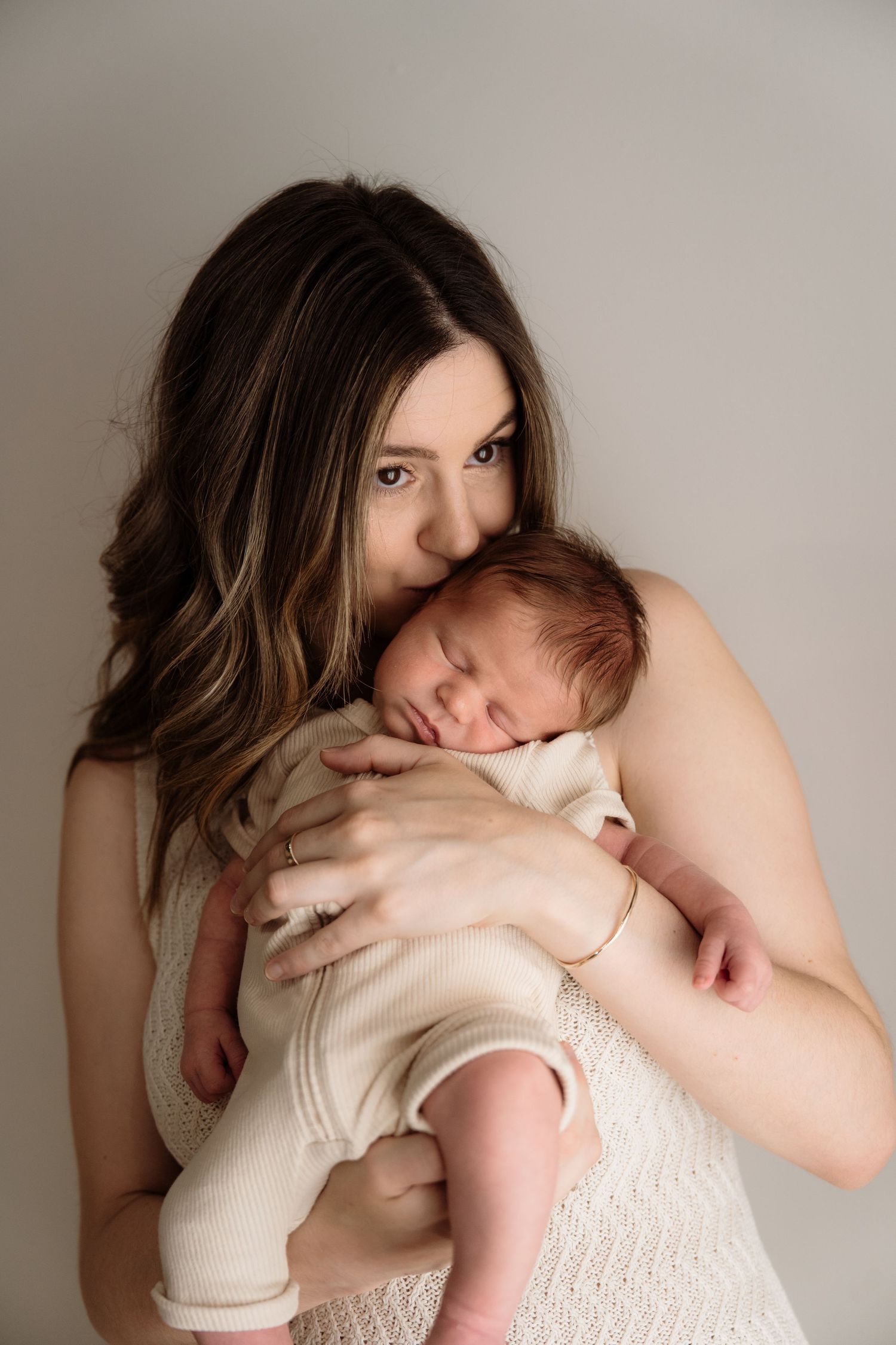 A tender embrace between a parent holding a sleeping newborn baby against their chest in soft white attire.