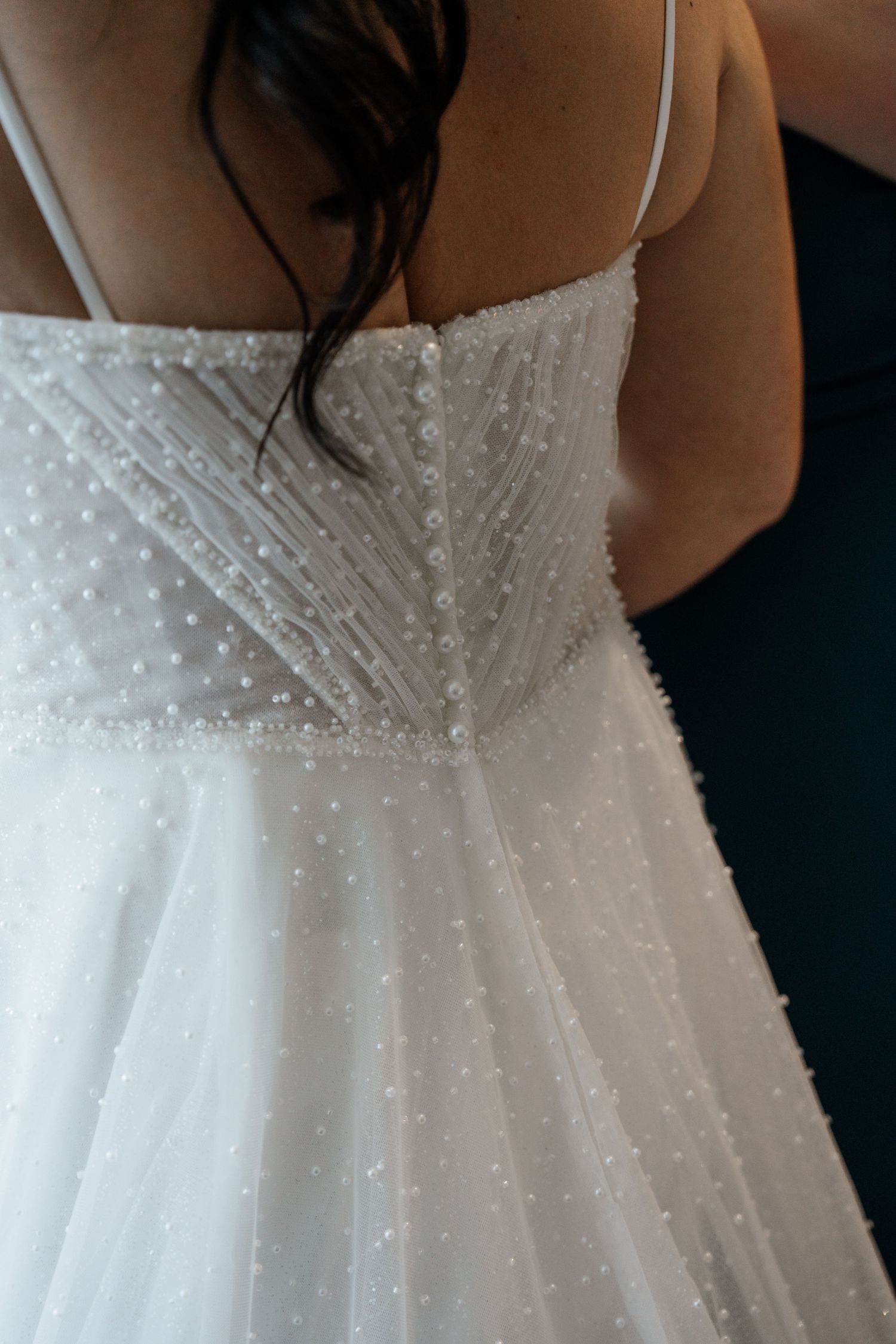 Close-up details of a white wedding dress with delicate pearl beading and pleated fabric texture.
