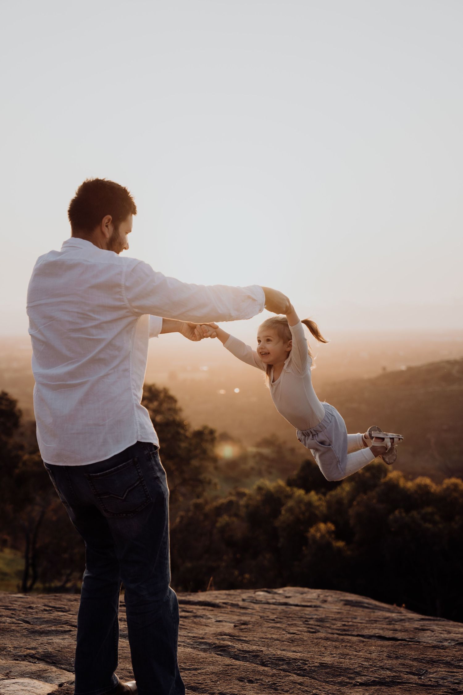 A couple silhouetted against a golden sunset sky dances together on a rocky mountain overlook.