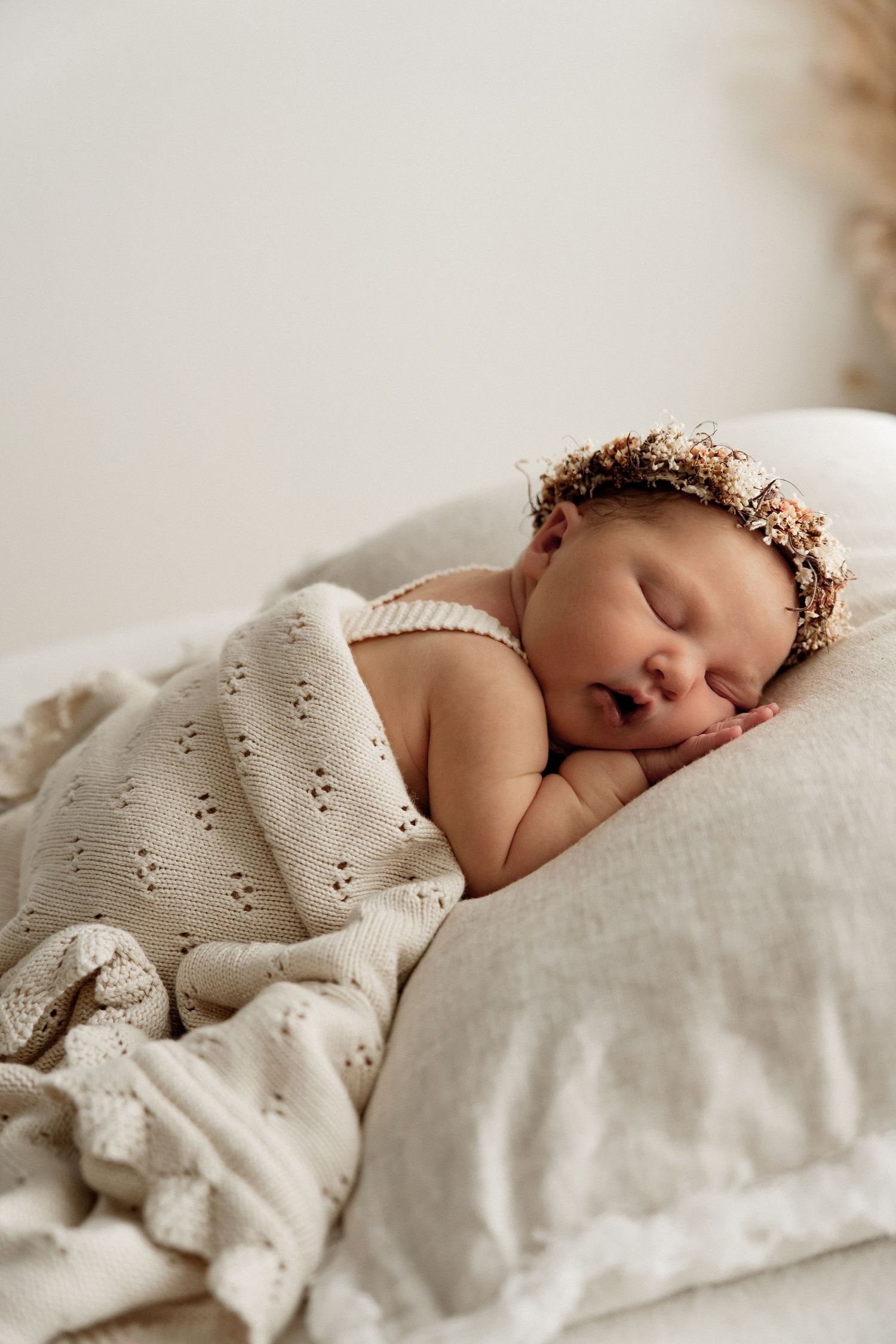 A peaceful sleeping newborn wrapped in a soft white textured blanket lies in dreamy natural light.