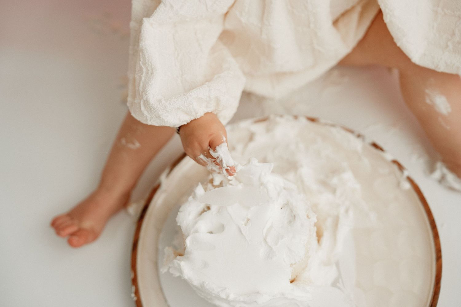 A small child's hands play with fluffy white shaving cream spread across a smooth surface during a sensory activity.