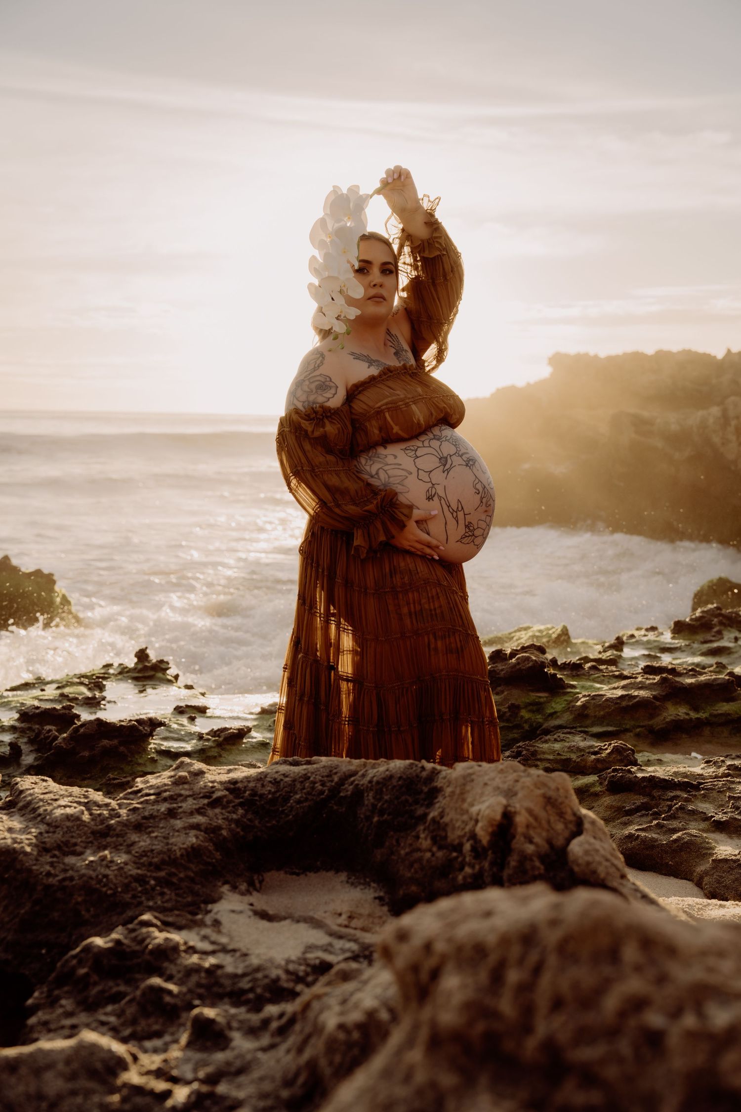 A figure in vintage dress stands on rocky coastal cliffs at sunset, creating a nostalgic silhouette against the ocean.