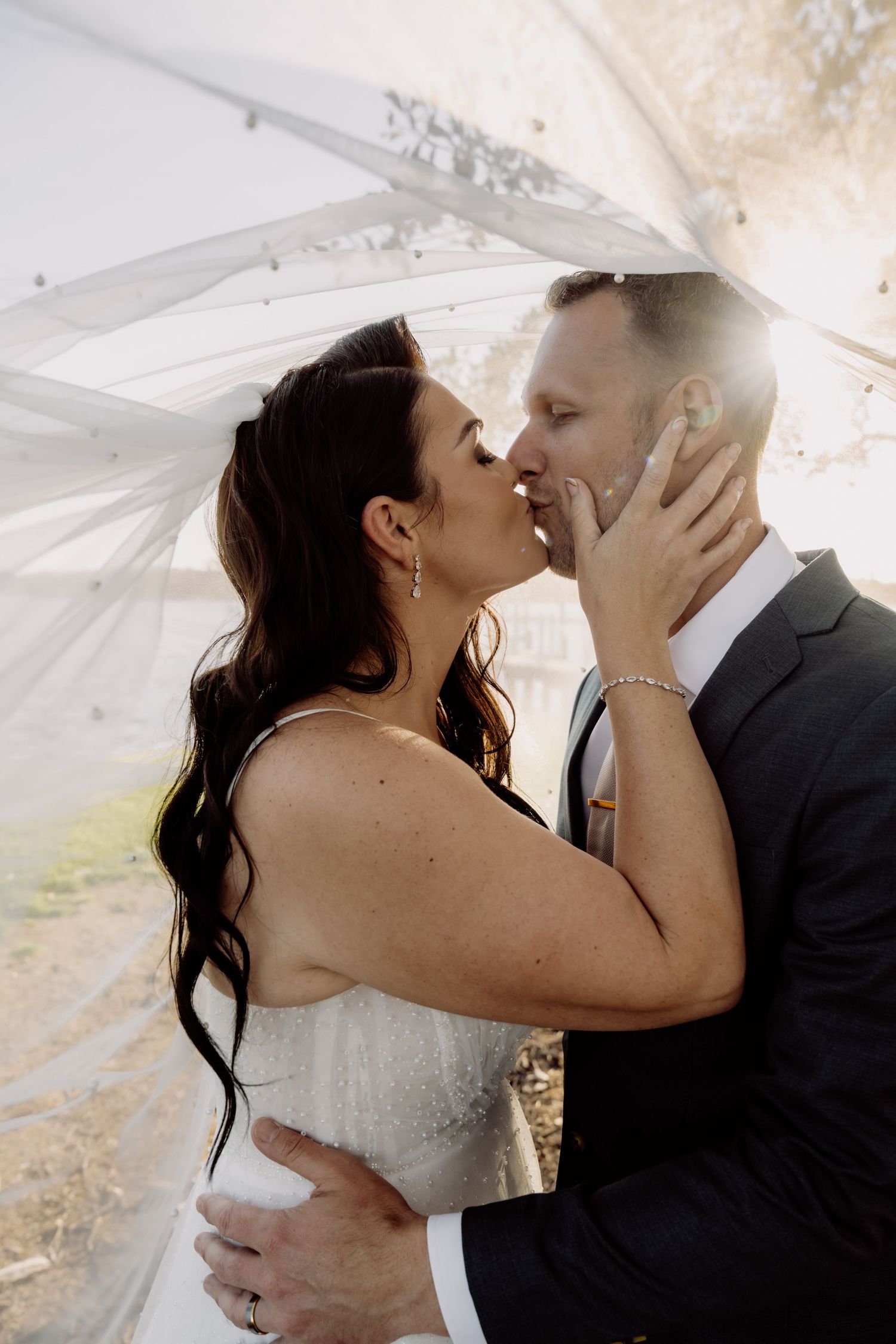 A romantic moment between newlyweds sharing a kiss under a white veil during their wedding ceremony.