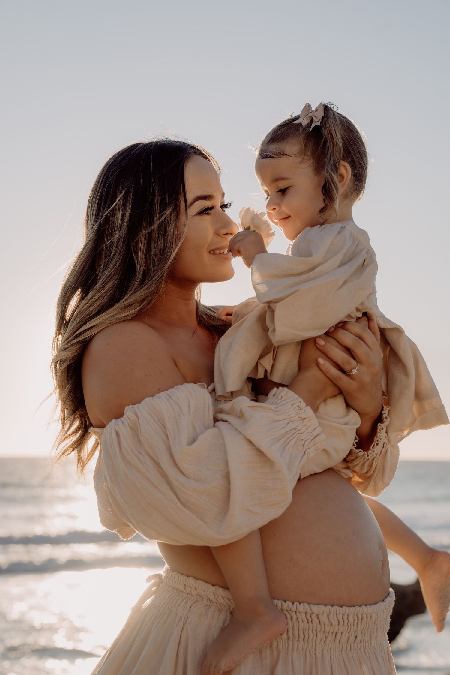 A series of heartwarming moments between a parent and young child in white outfits playing together at sunset on the beach.