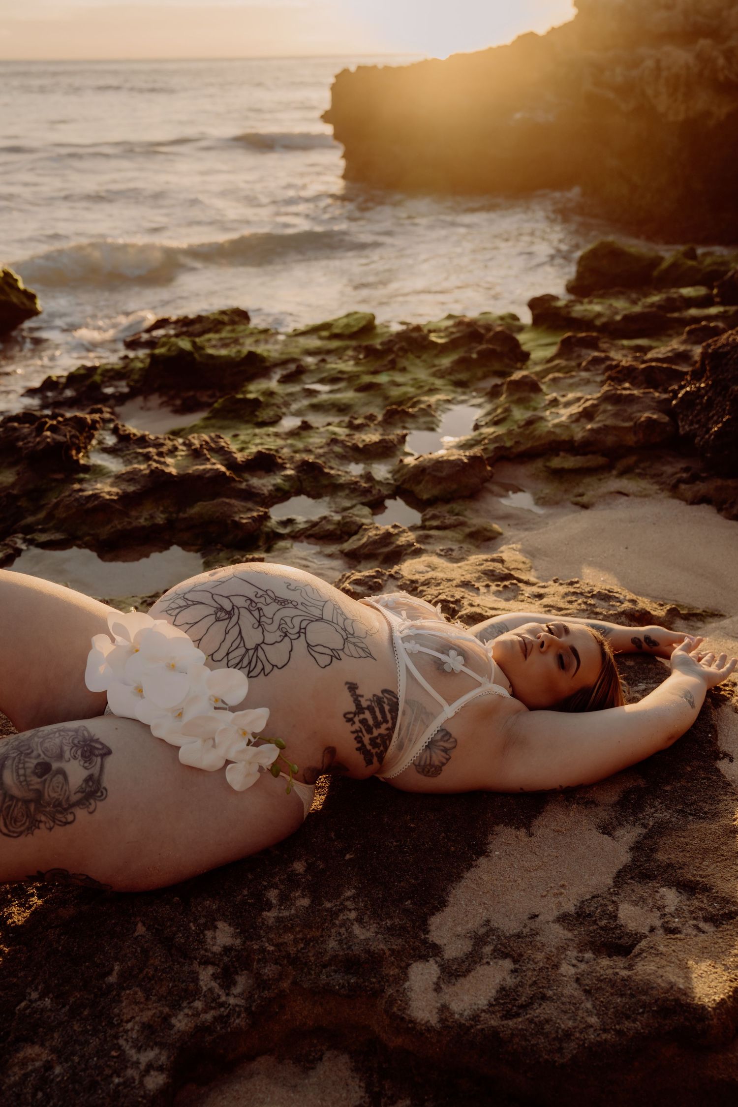 Artistic beach photoshoot at sunset with waves crashing on rocky shore.