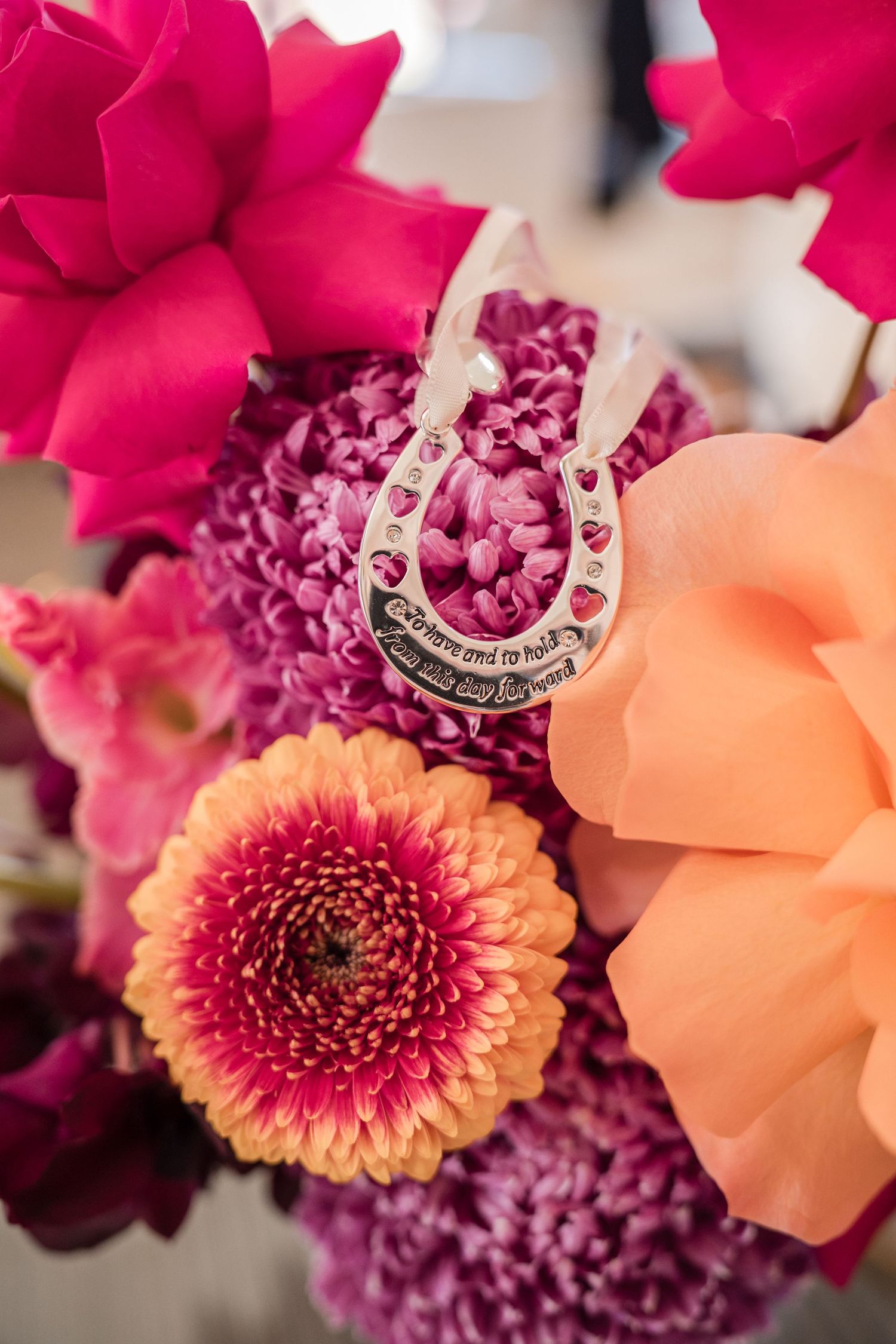 Close-up of a pink and orange floral arrangement with dahlias and roses showcasing a silver ring.