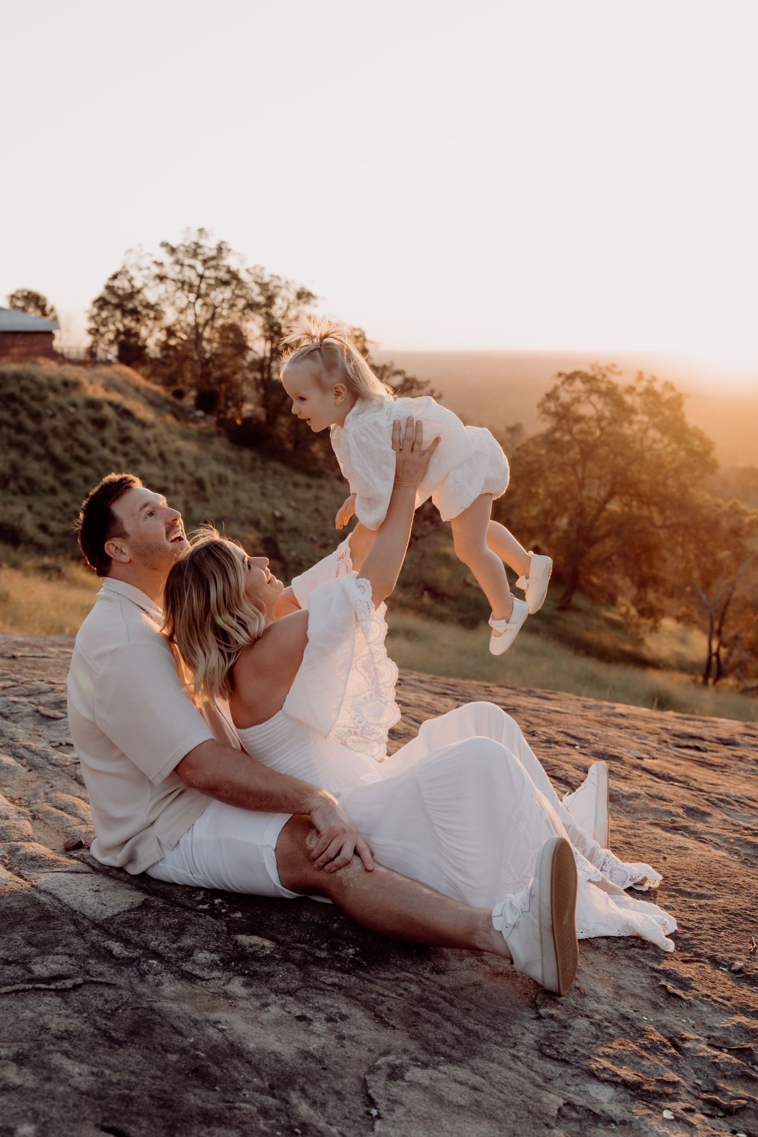 A couple in white outfits share intimate moments at sunset on rocky terrain in a series of romantic photos.