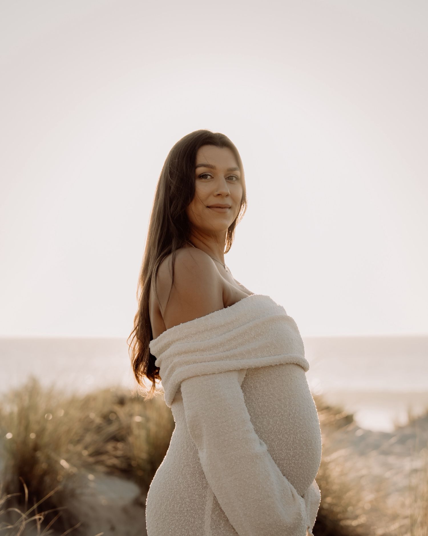 A woman wrapped in a cozy white blanket poses outdoors during golden hour in a desert landscape.