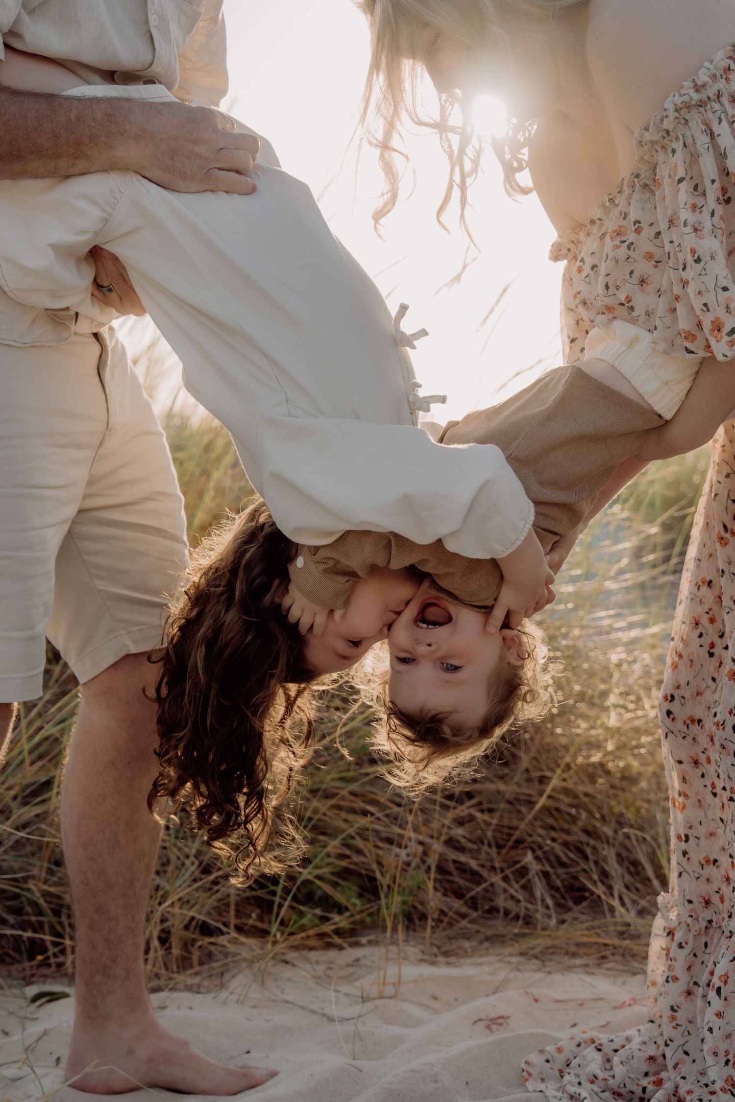 A romantic couple in white clothing shares an intimate moment on a sandy beach at sunset.