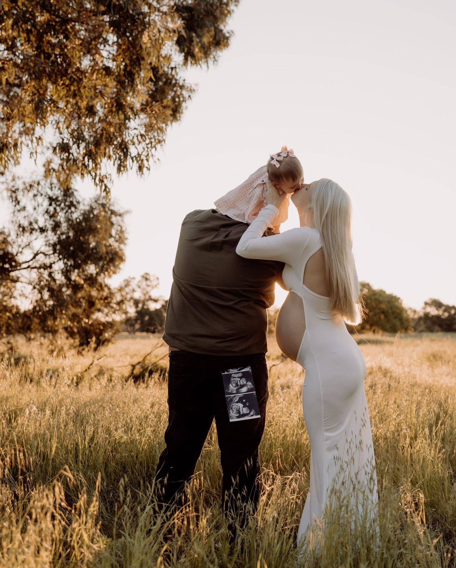 Silhouetted couple sharing an intimate moment in a golden sunlit meadow at sunset.