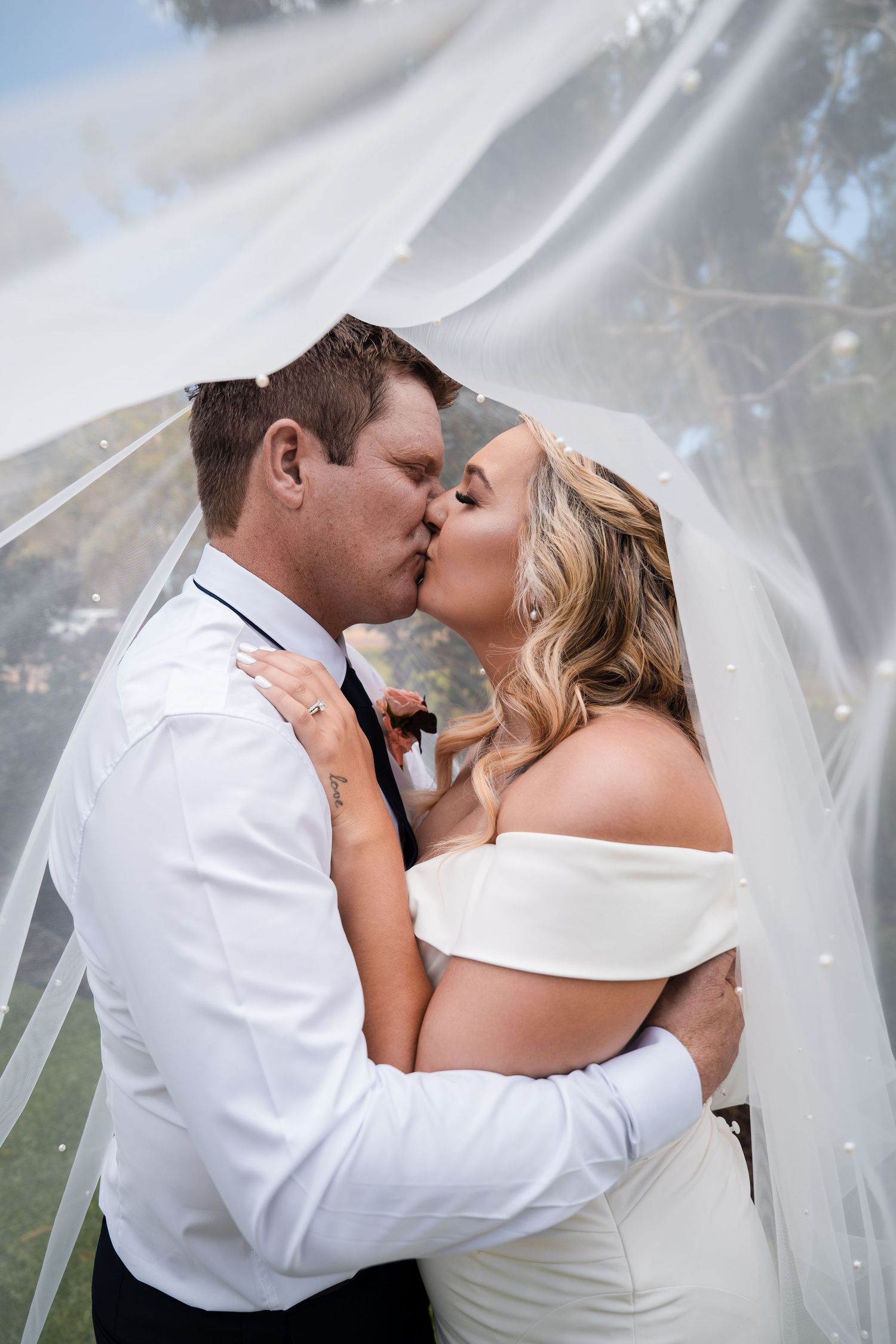 A romantic wedding couple shares a tender kiss under a flowing veil in a series of four similar photos.