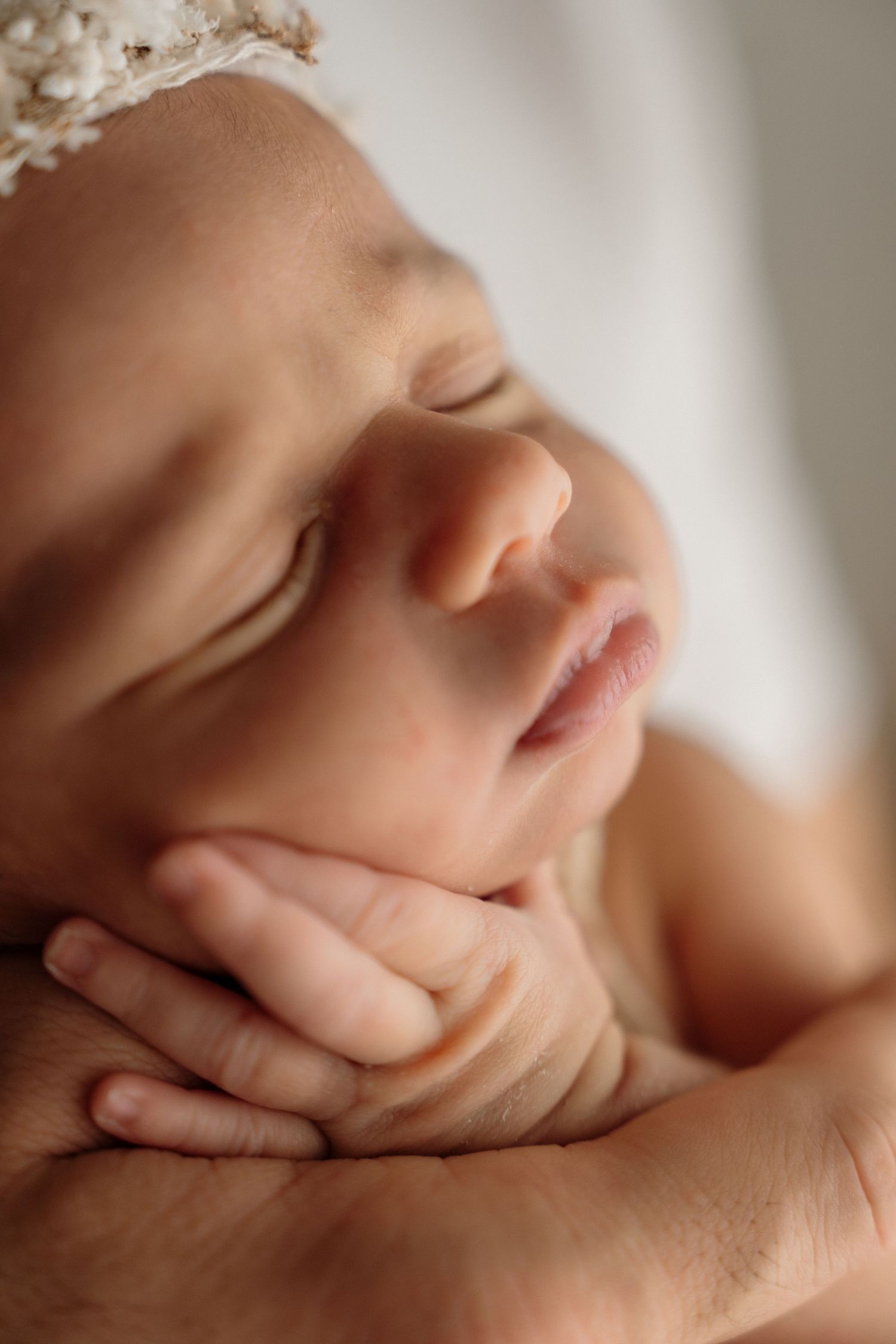 Peaceful sleeping newborn with delicate lace headband rests gently in parent's supportive hands.