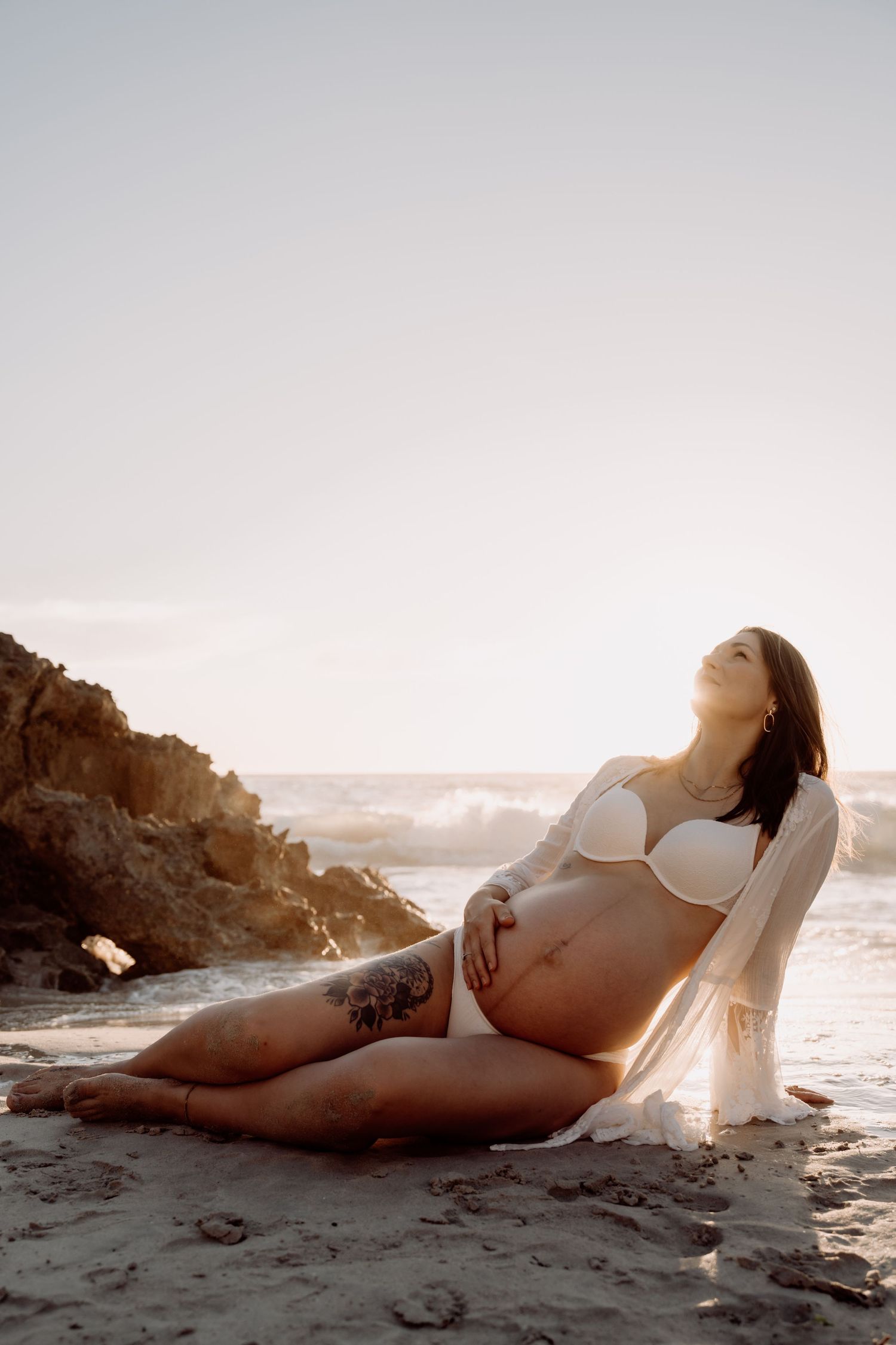 Artistic black and white boudoir photos of a person posing on a beach at sunset.