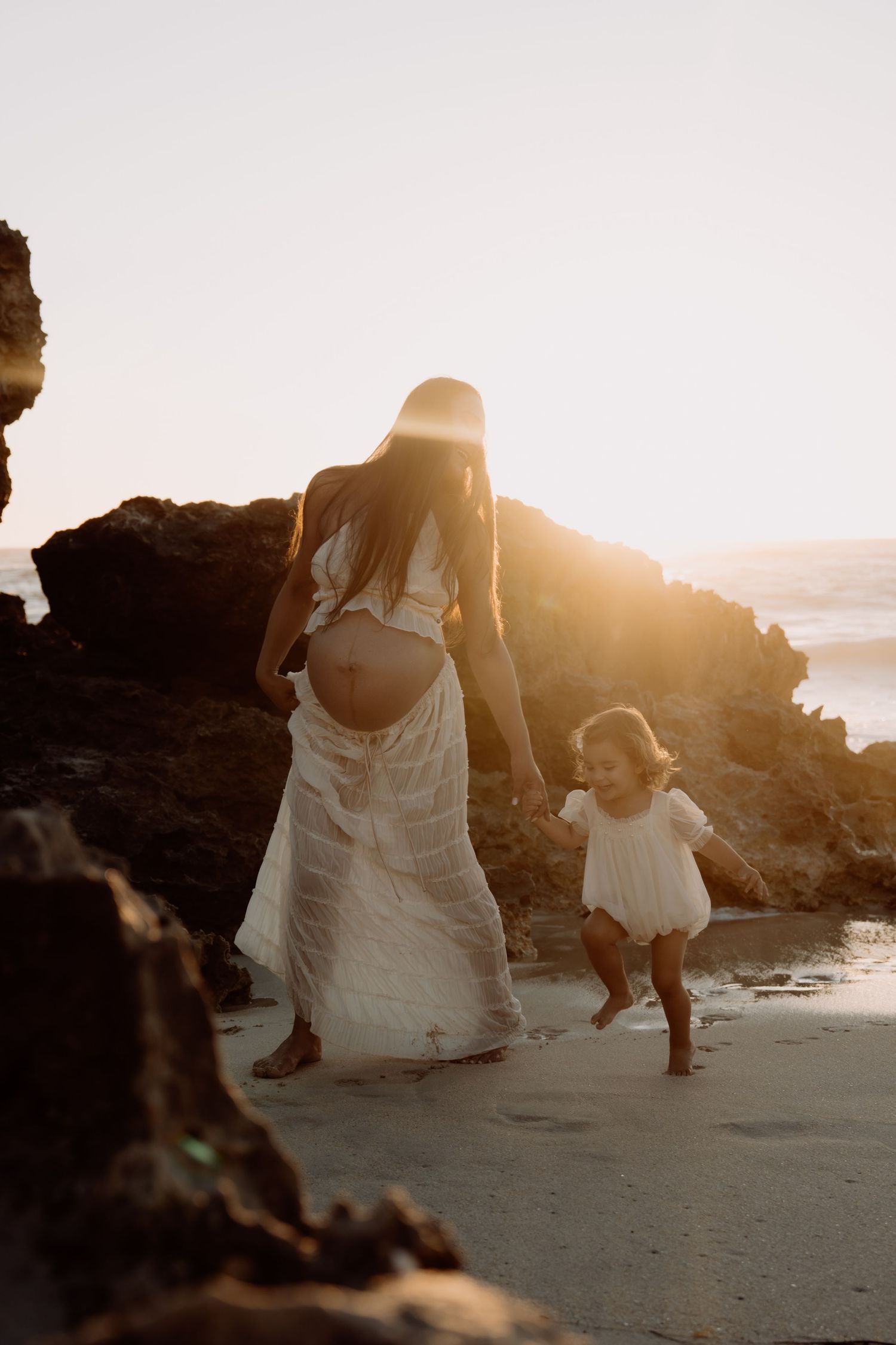 Silhouettes of people walking along a beach at sunset with golden light filtering through the rocks.