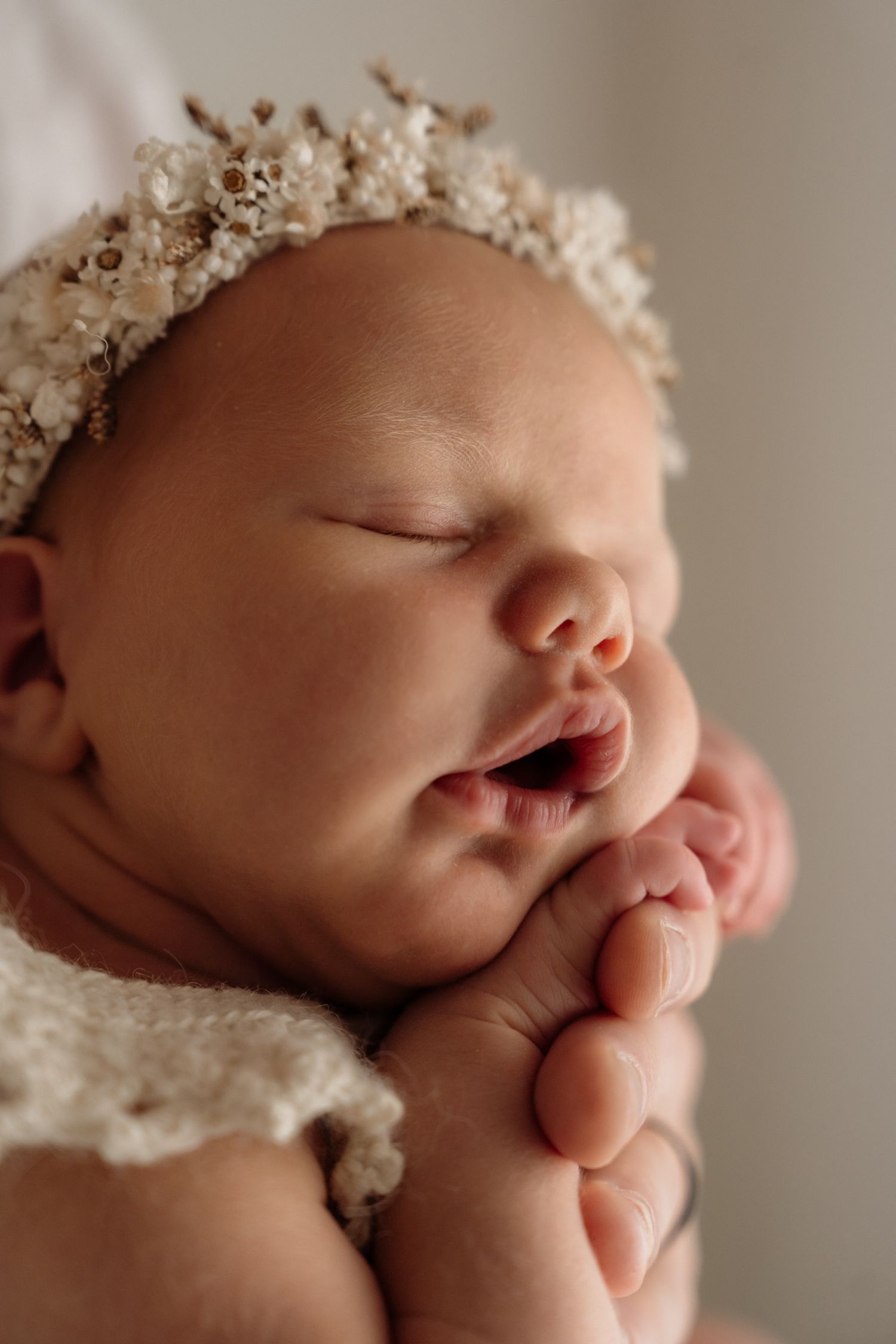 Close up of sleeping newborn baby wearing white lace headband in delicate professional studio portrait series.