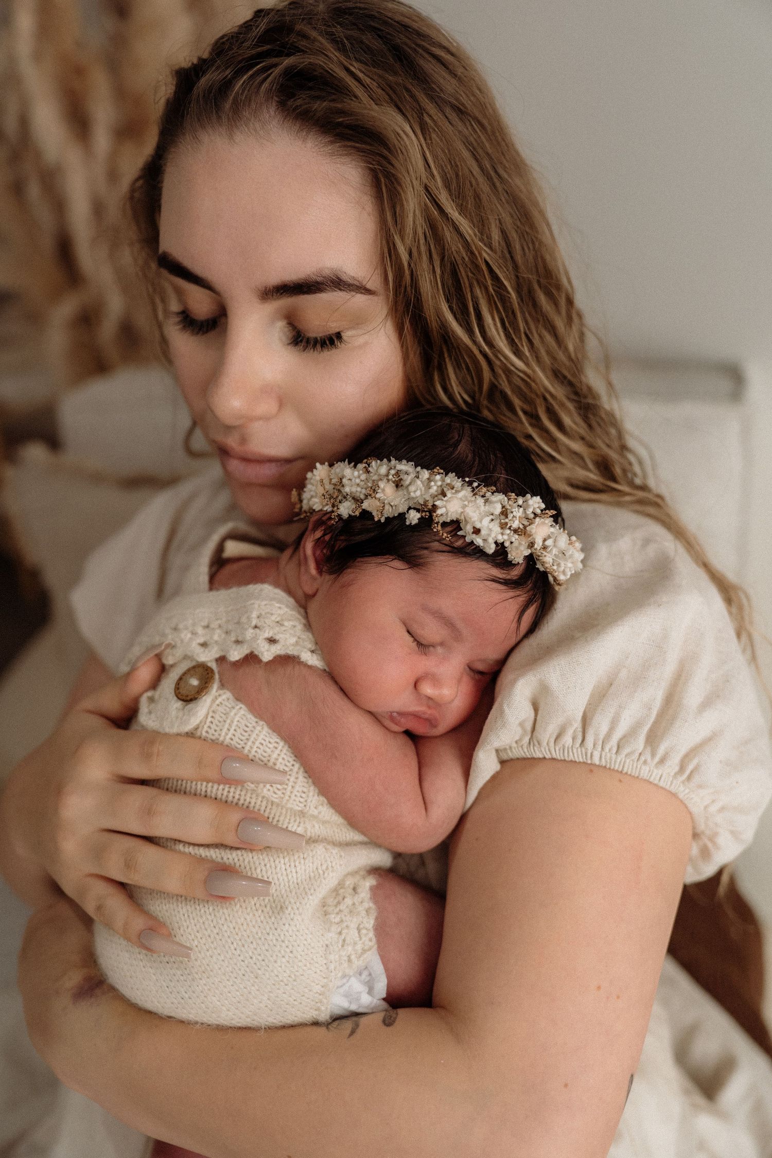 A tender series of maternal moments captured in warm tones as parent embraces sleeping baby in cream bonnet against neutral backdrop.