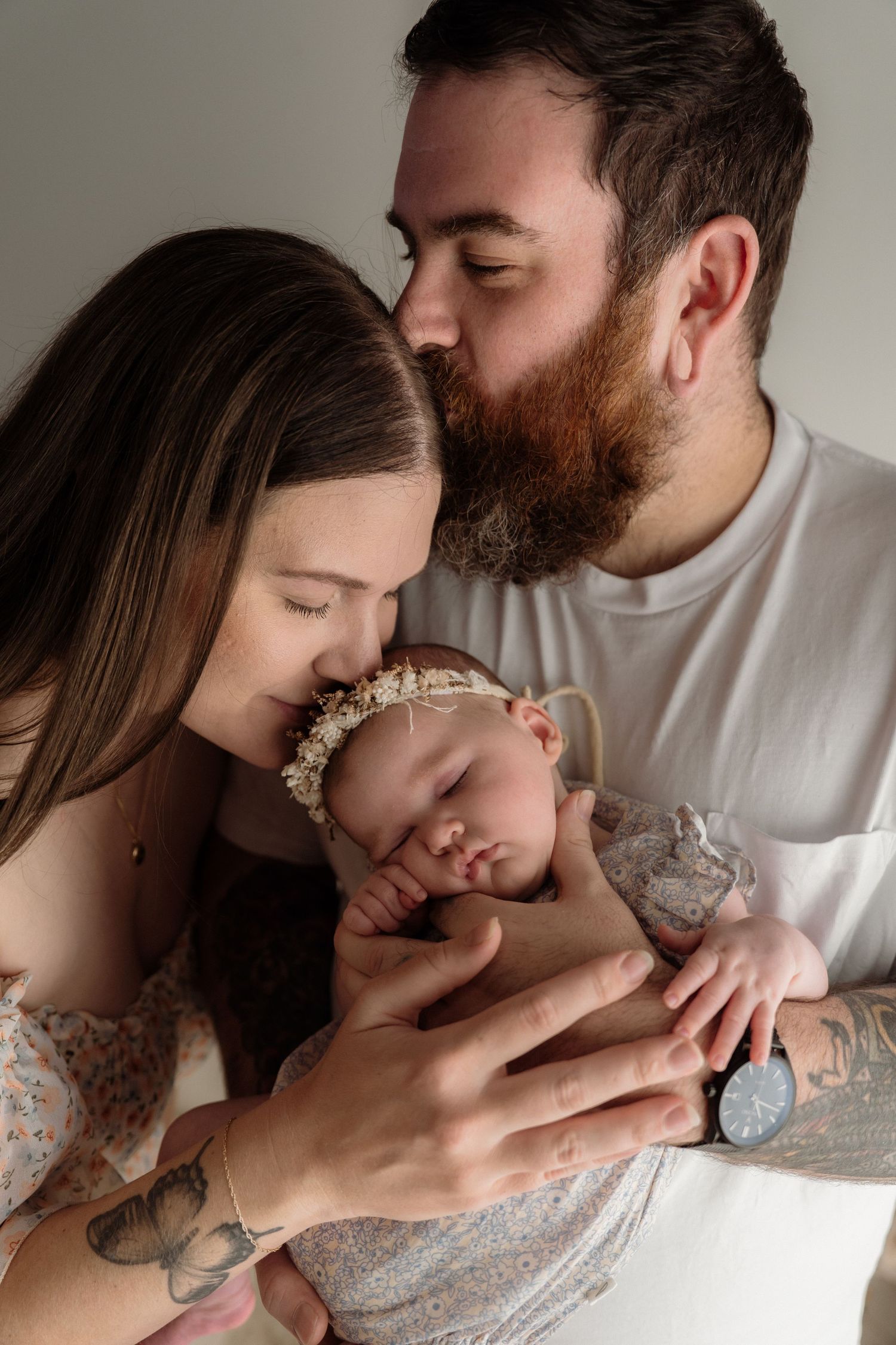A tender family moment shows parents lovingly cradling their sleeping baby wearing a floral headband.