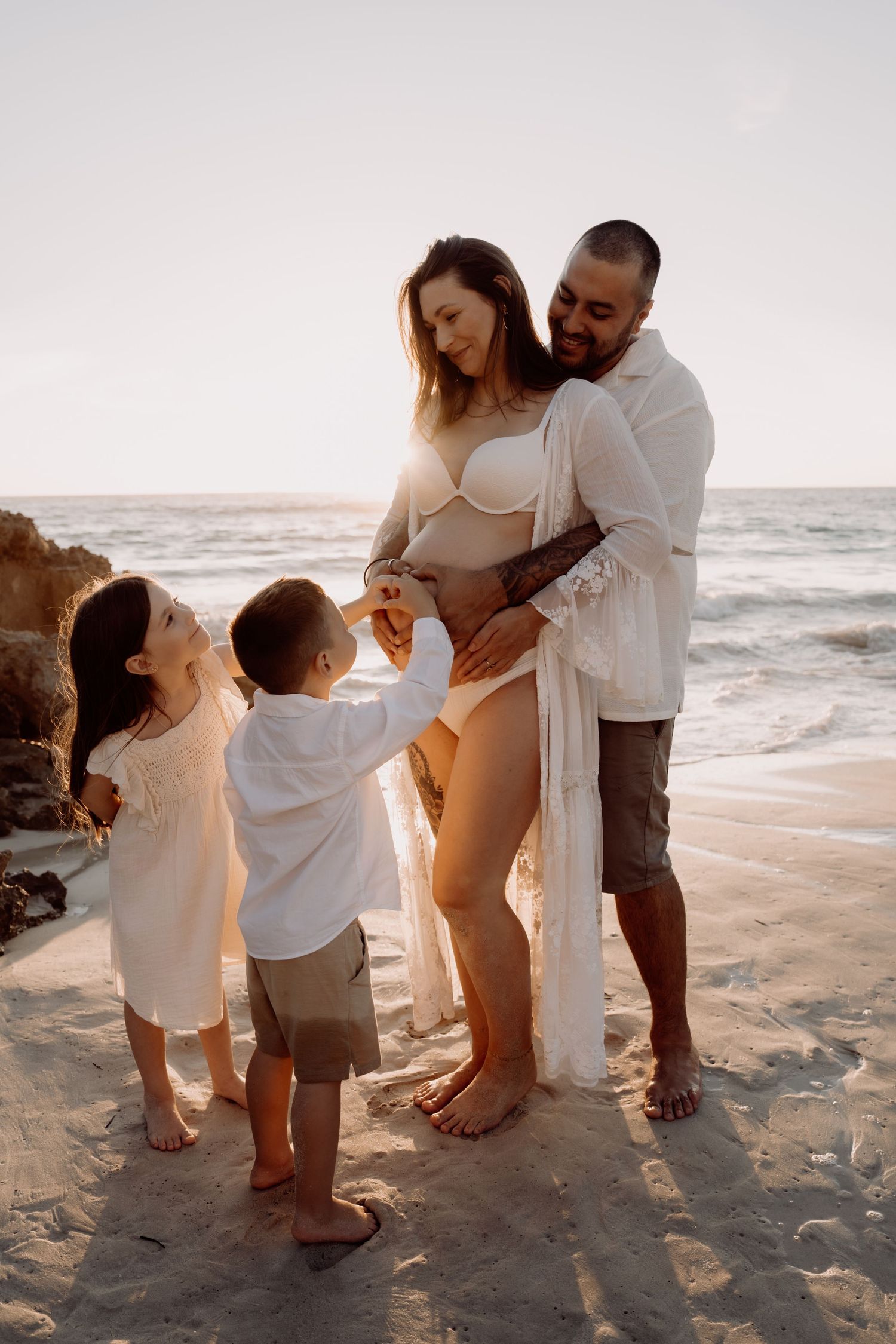 A family shares intimate moments on a sandy beach at sunset, capturing their maternity journey in a series of photos.