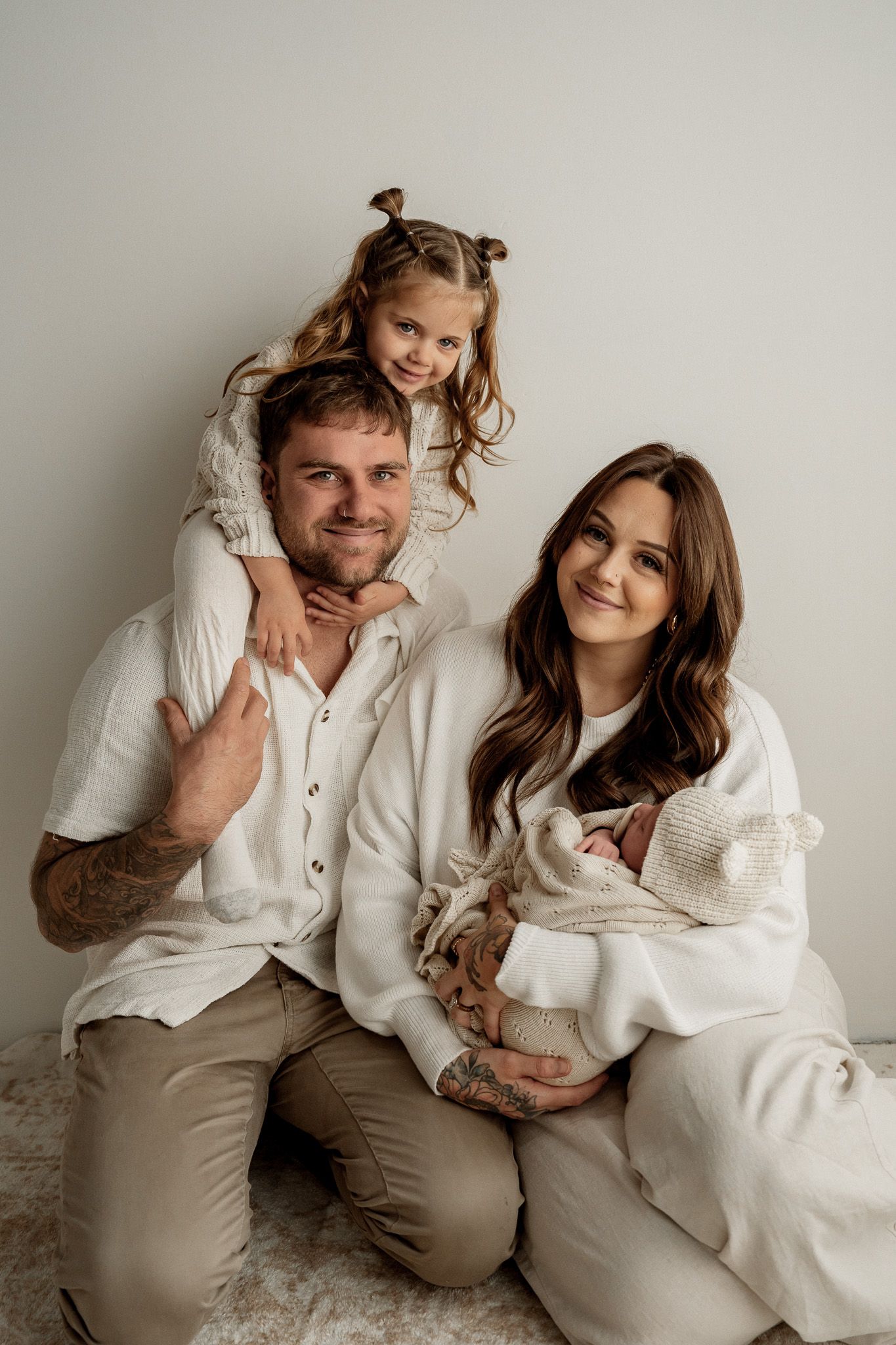 A loving family in neutral white outfits poses together for an indoor portrait session.