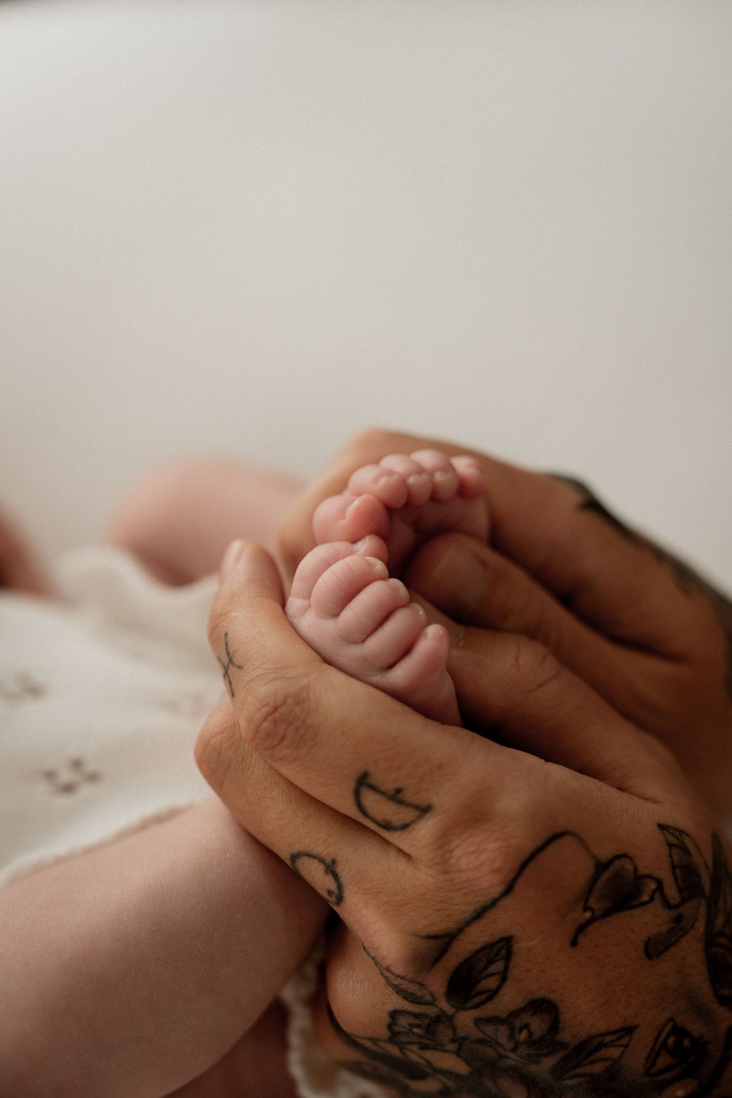 Close-up of holding hands showing intricately tattooed skin with delicate artwork designs against a soft white background.