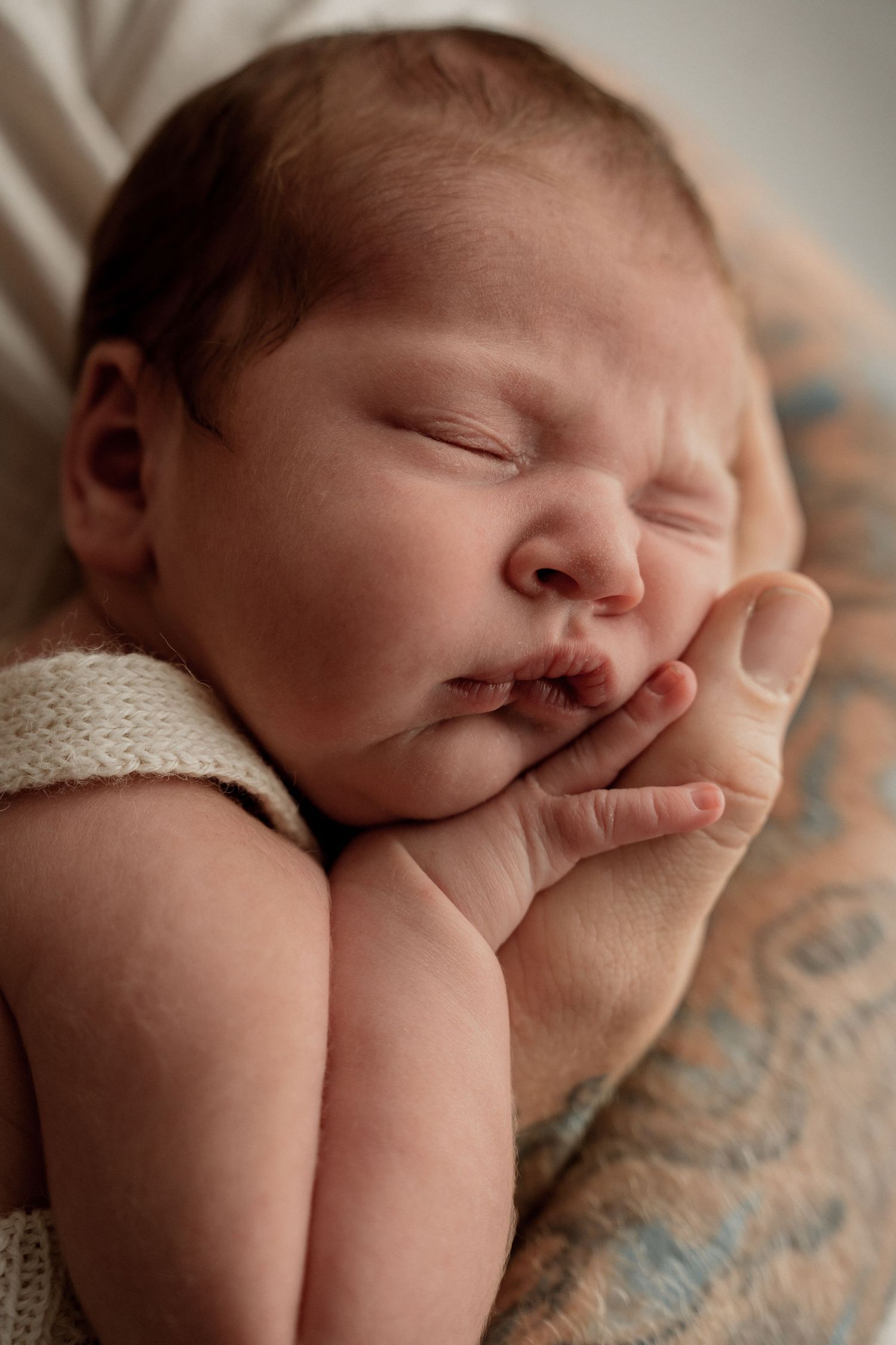 A sleeping newborn baby rests peacefully on a cream and blue blanket.