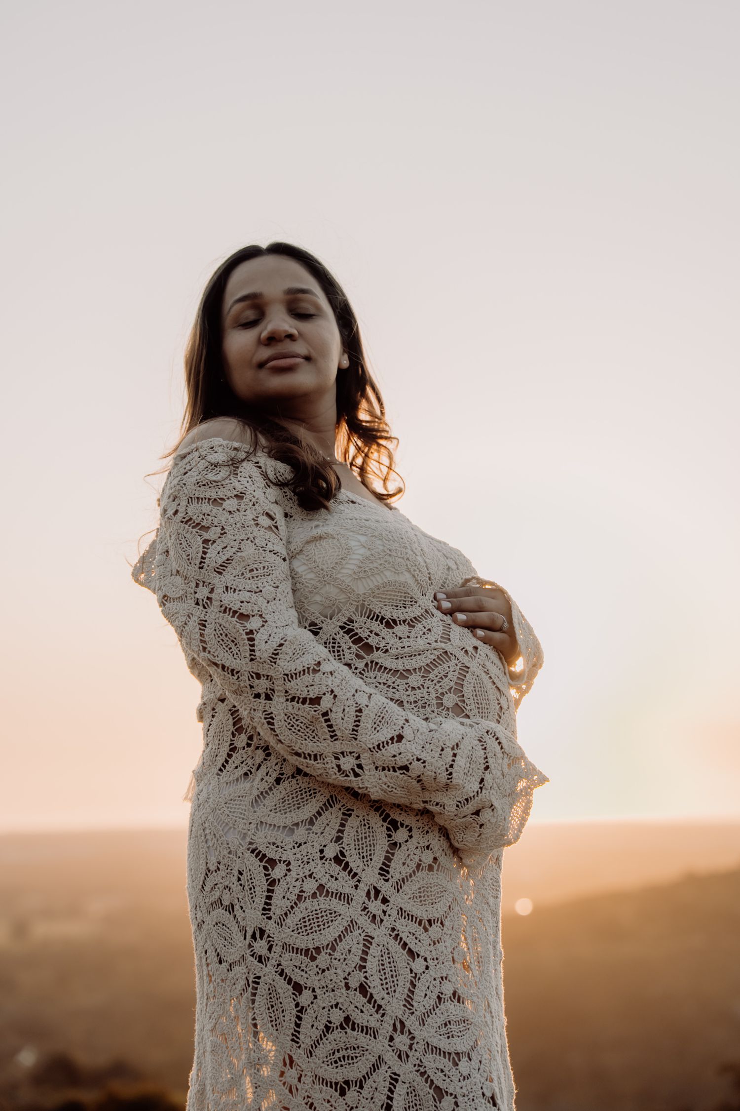 Someone wearing a cozy lace shawl poses against a warm sunset backdrop, creating a dreamy silhouette effect.