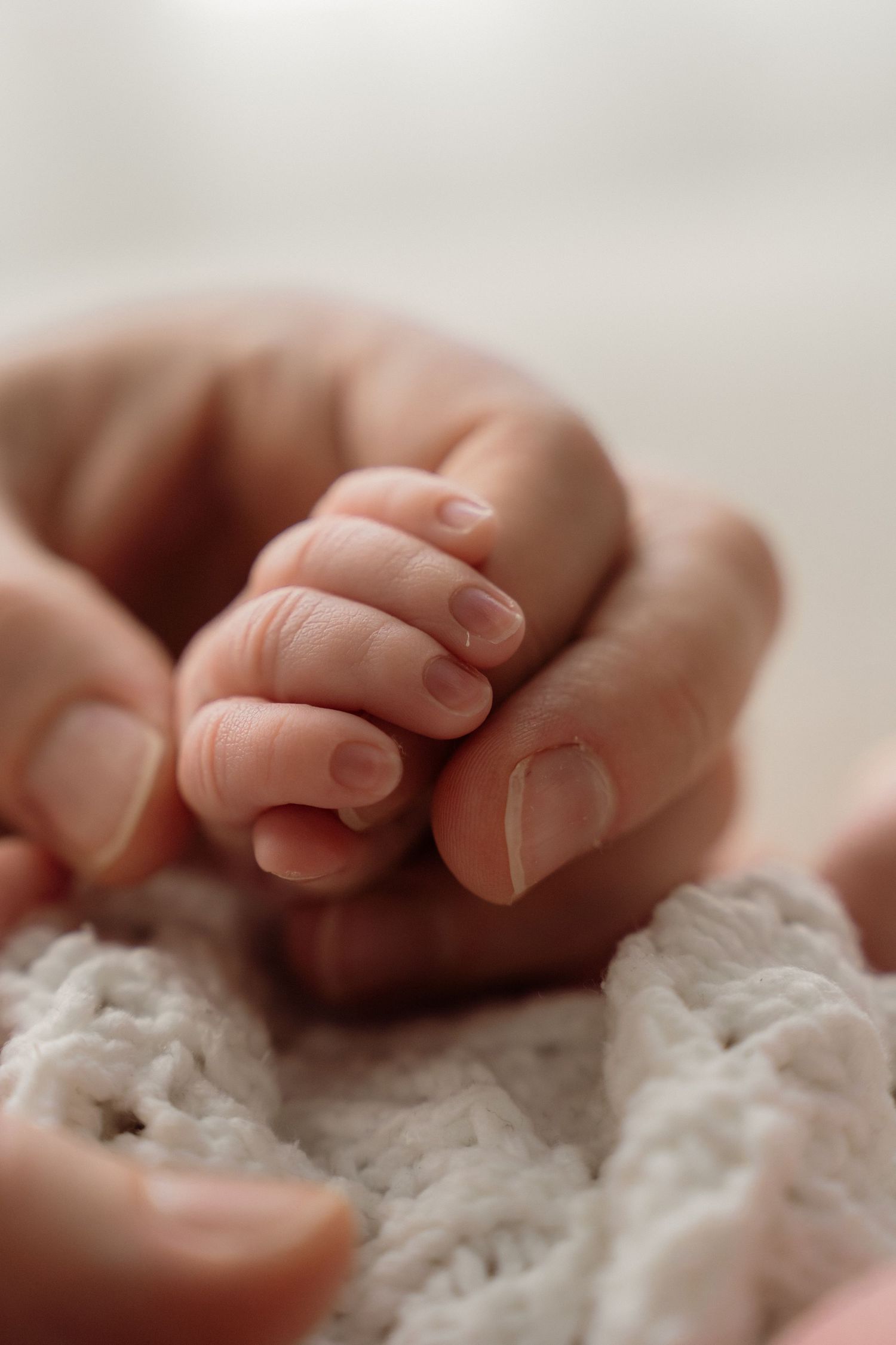 A close-up of tiny baby fingers grasping soft white fabric in a tender, gentle moment.